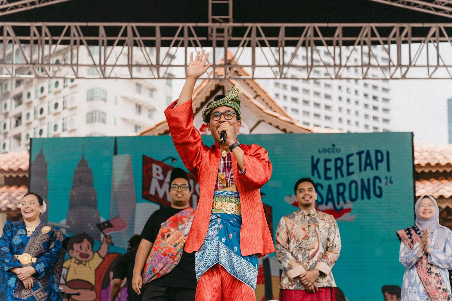 Performer in vibrant orange attire energetically entertaining the crowd on an outdoor stage.