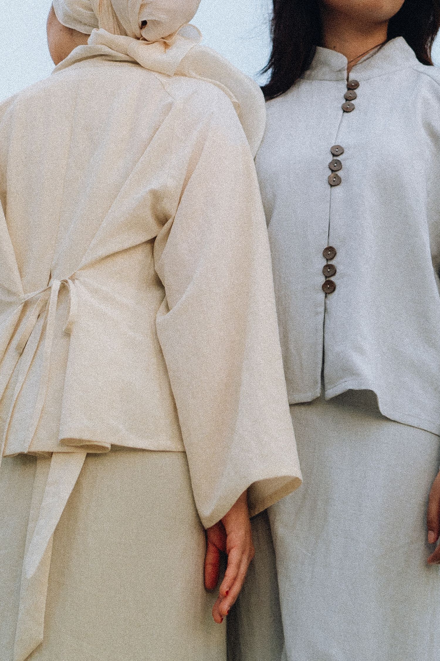Close-up detail of two outfits in cream and white tones with decorative buttons.