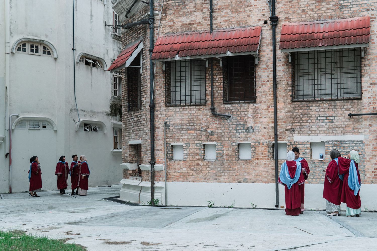 People in red robes gathering in front of a brick building with arched windows.