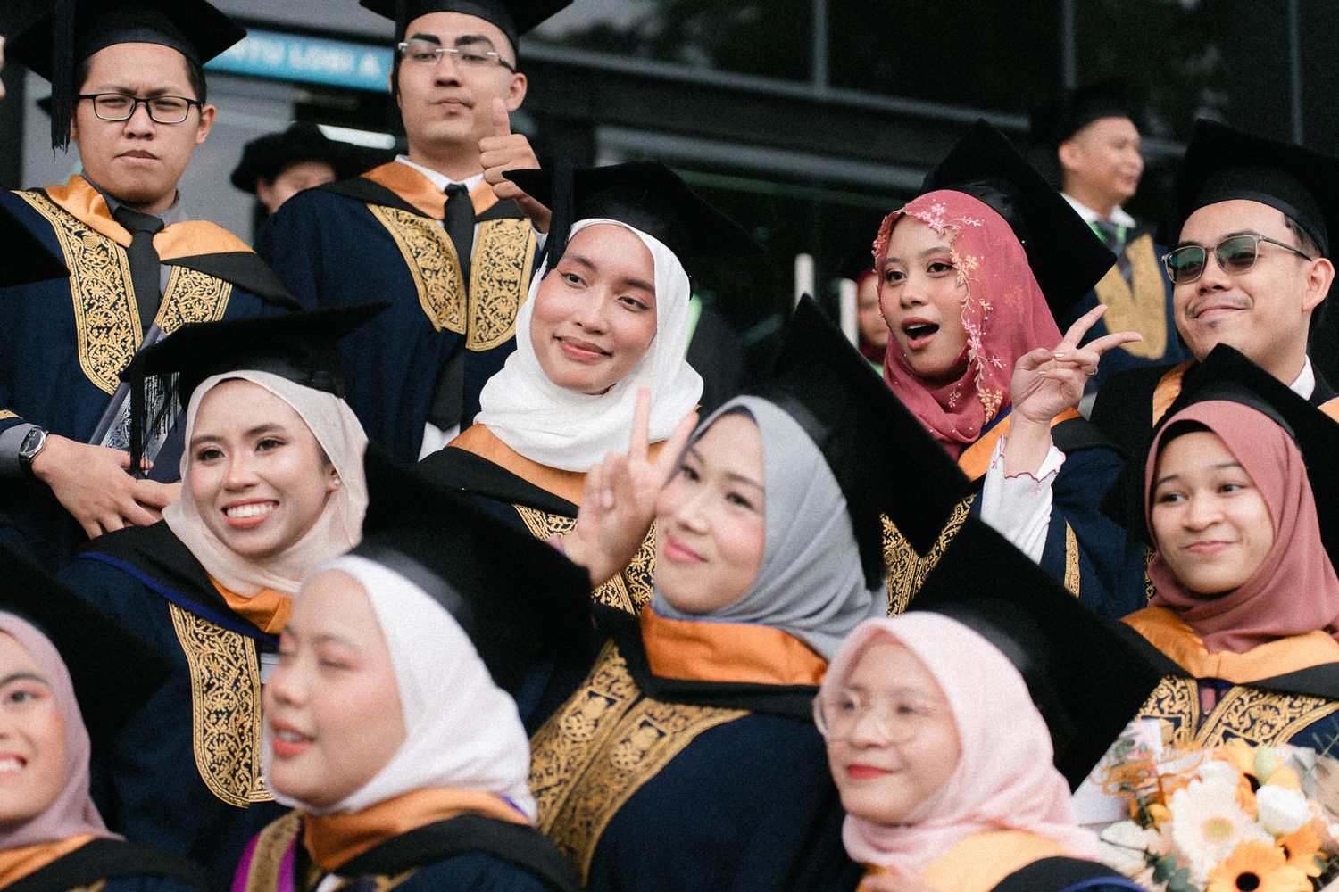 Group of graduates in black and gold academic robes and hijabs smiling and posing for a graduation photo.