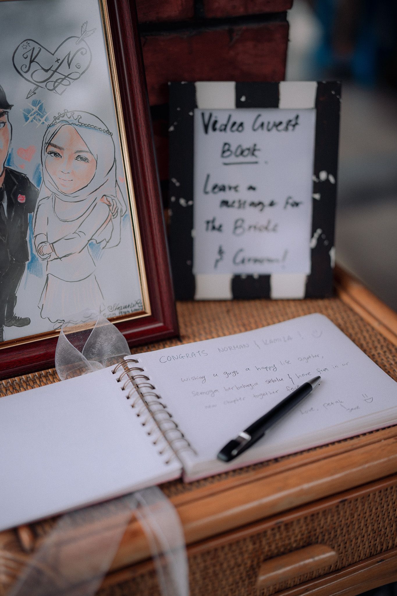 Wedding guest book display with cartoon bride illustration, open notebook with pen, and video message sign on wooden table.
