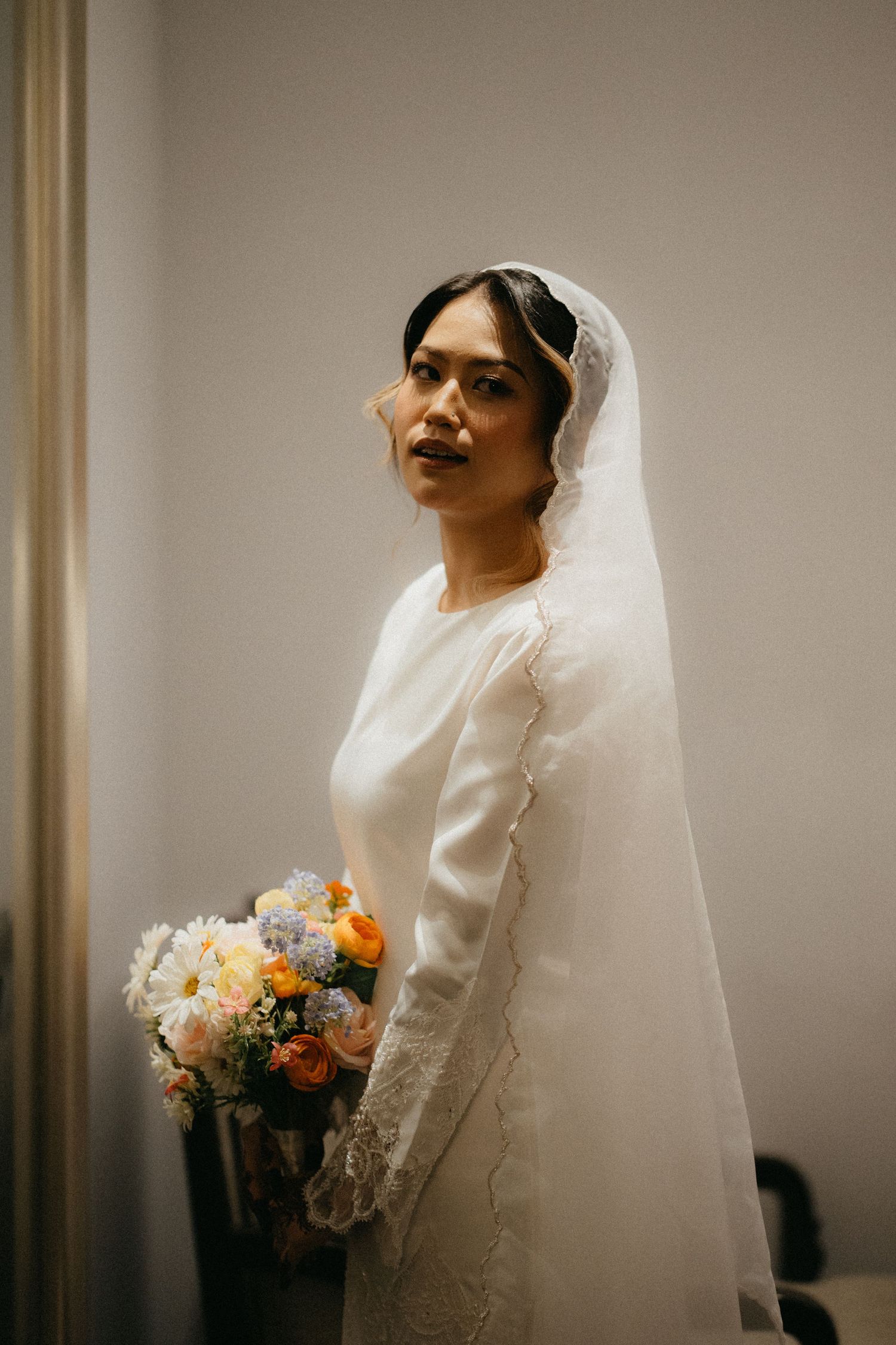 Bride wearing a flowing white veil poses with a soft peach and cream floral bouquet in elegant wedding portraits.