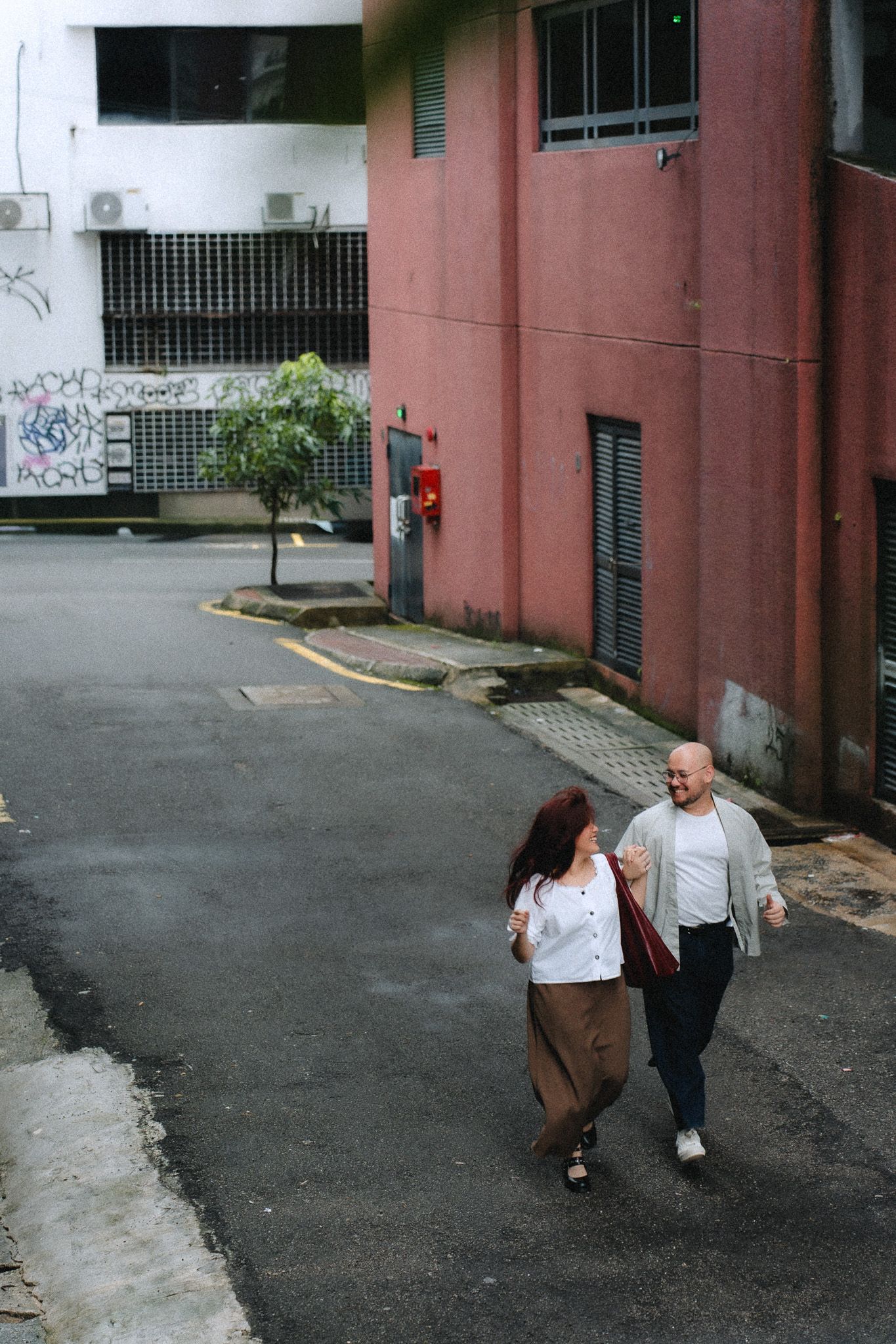 Couple walking together on an urban street beside a pink building with graffiti walls in the background.
