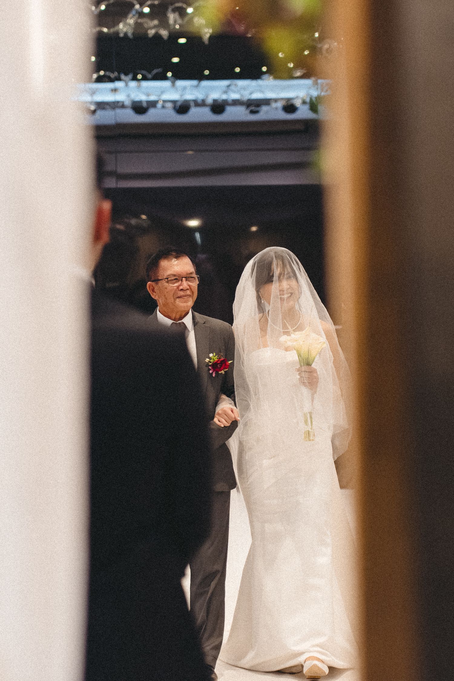 A bride in a white gown stands with someone in formal attire during an indoor wedding ceremony.