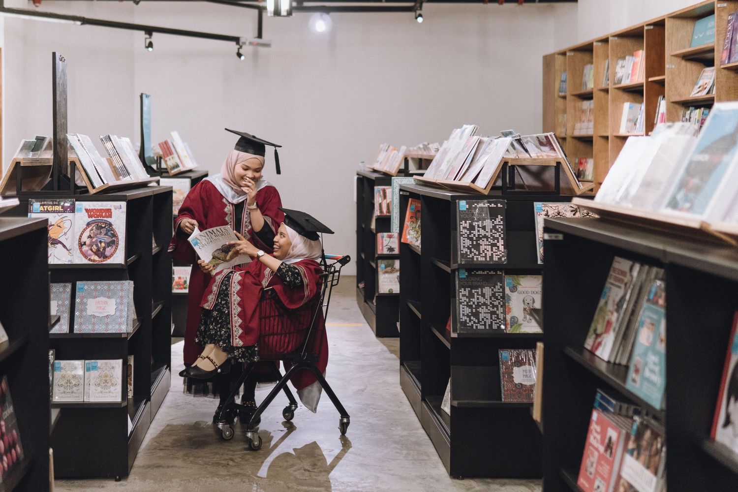 A graduate in red regalia browses books between dark library shelves.
