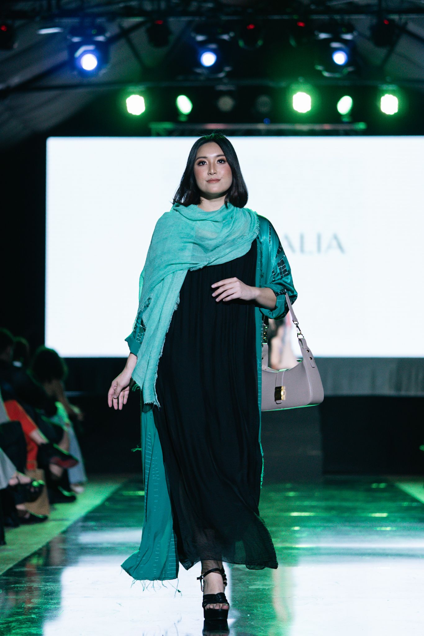Fashion model walks runway in black and teal modest dress with matching scarf.