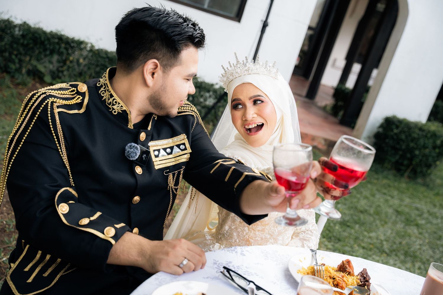 A couple in formal attire share red drinks at an elegant outdoor dining setup.