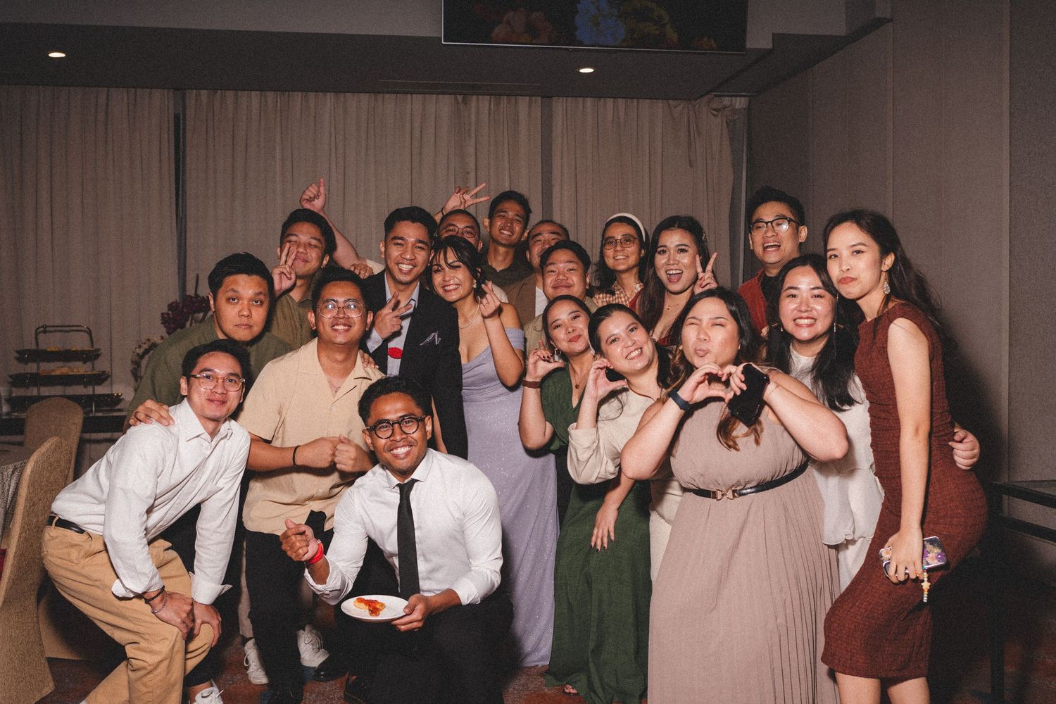 A lively group of party guests posing together at an indoor event with formal attire.