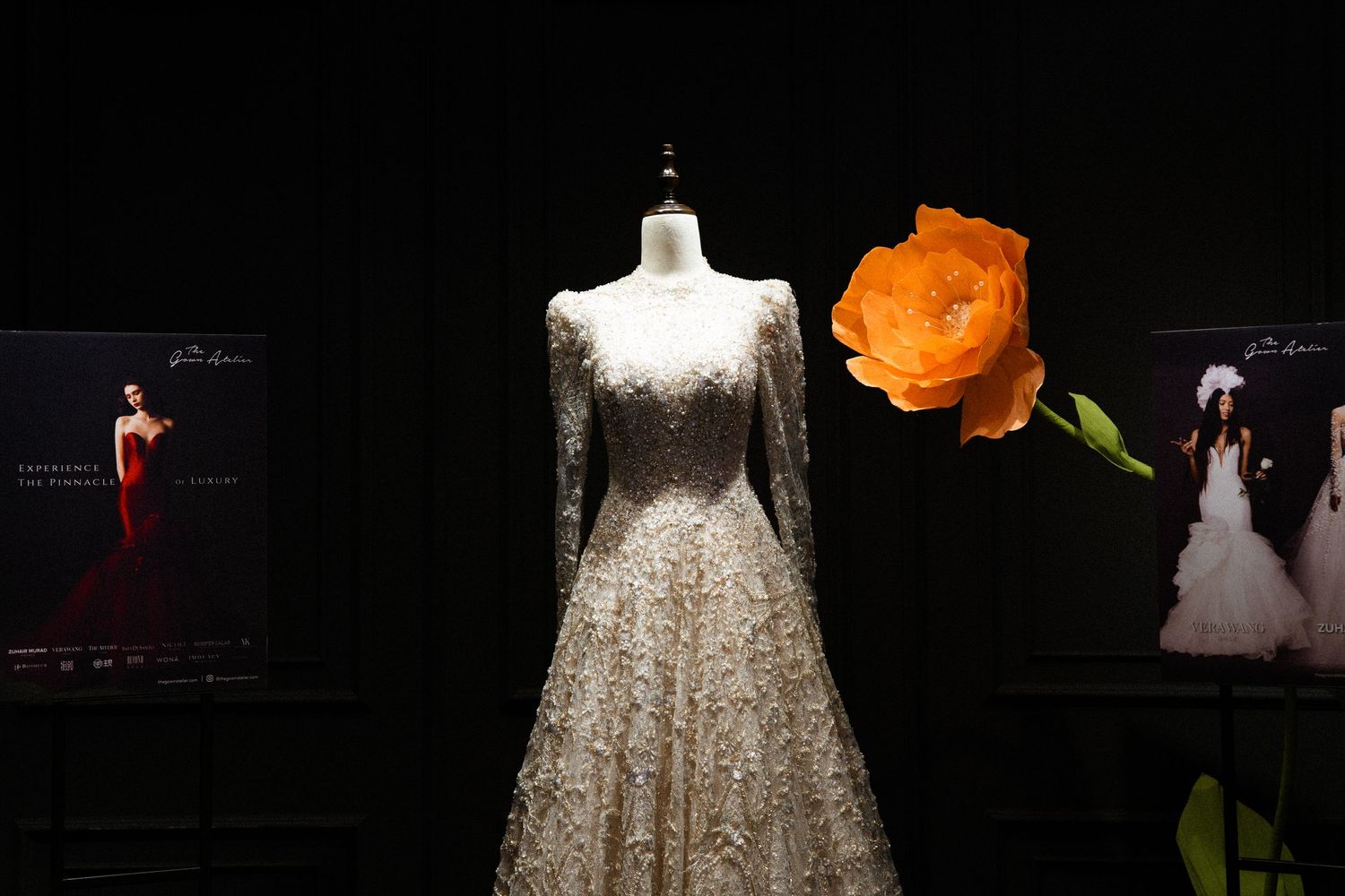 Sparkling sequined wedding dress on display with an orange rose accent against a black background.