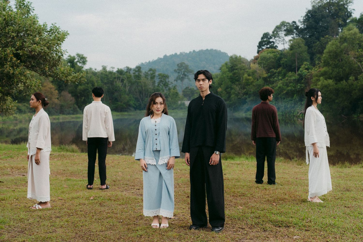 Models in minimalist white and blue clothing standing in grassy field with mountains behind.