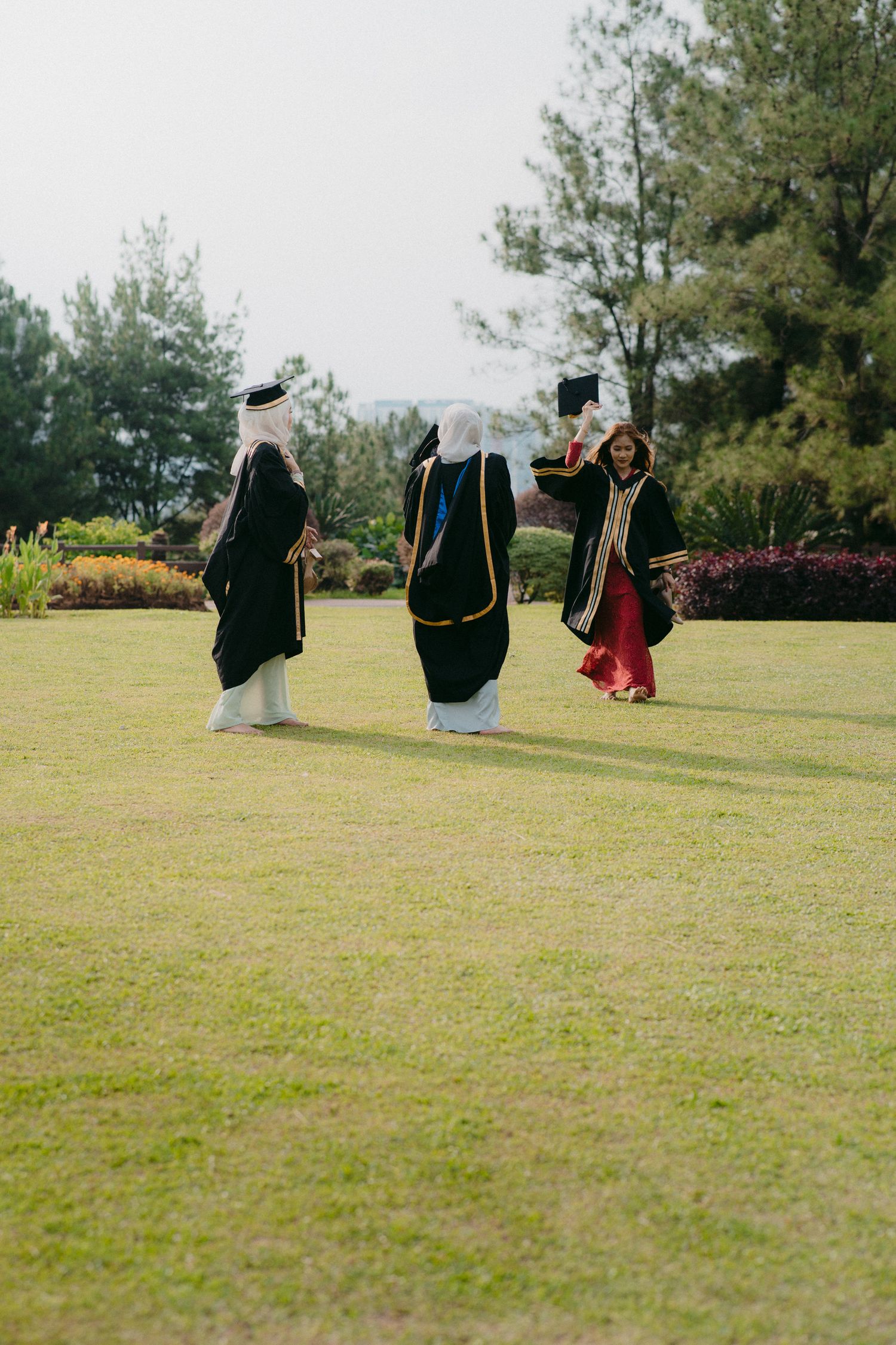 Three graduates in black robes jumping for joy on a sunny lawn.