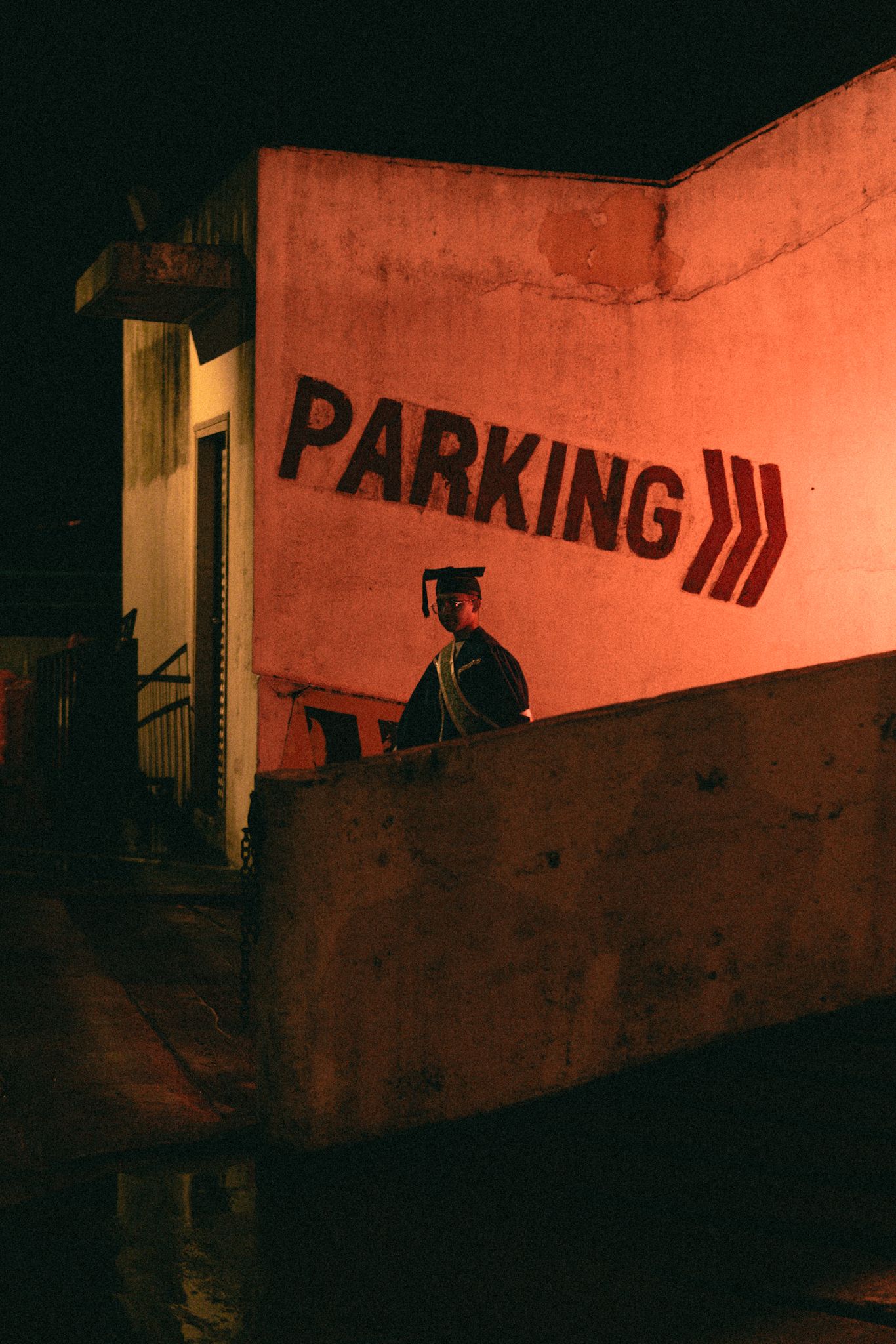 Dark silhouette against red wall with parking sign and moody night lighting.