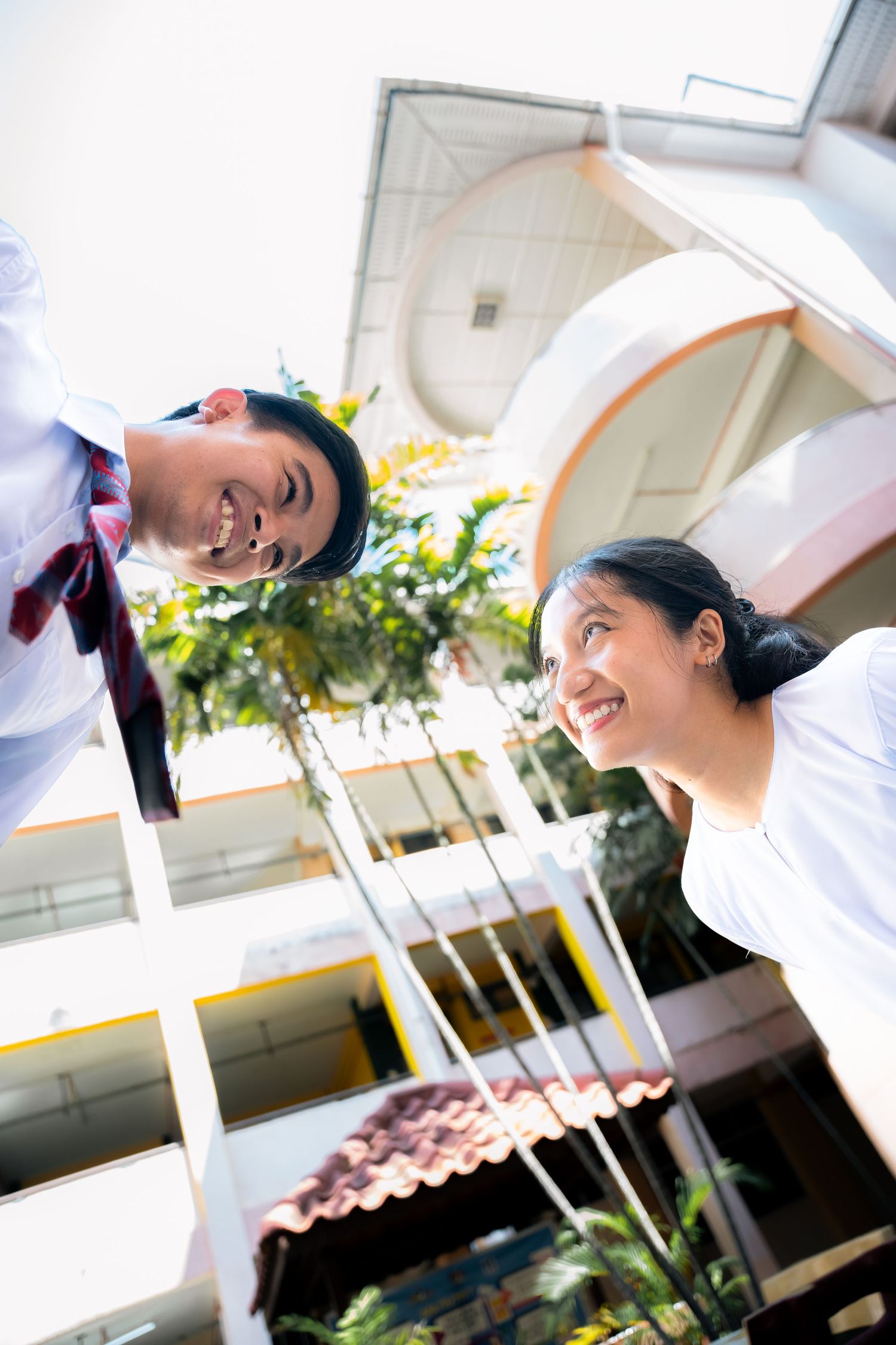 Two people in white shirts smile at each other from different levels of a building with arched architecture.