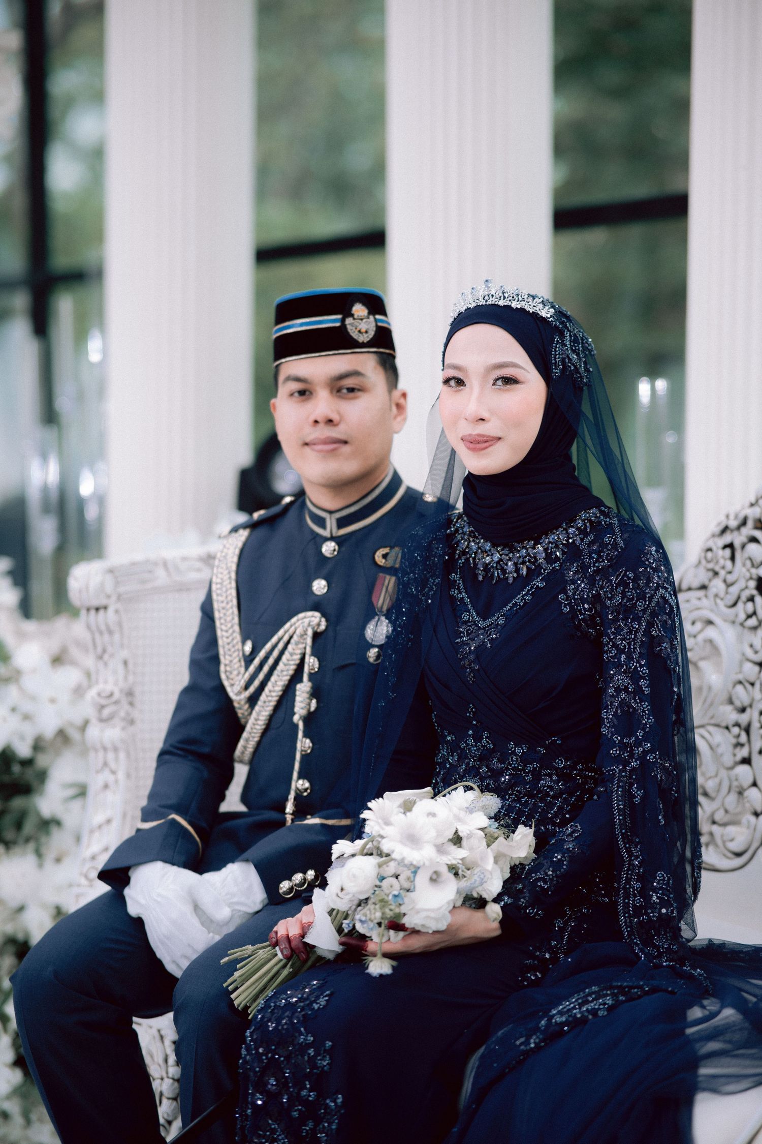 Traditional Malay military wedding photo featuring formal attire with navy uniform and dark blue embellished dress with hijab.