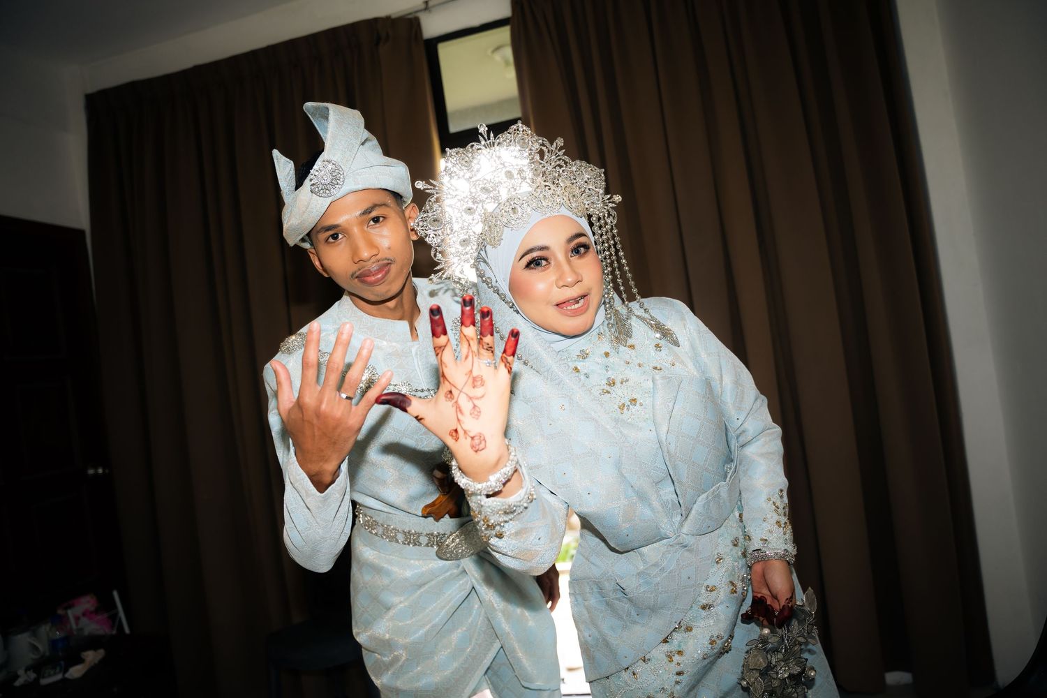 A smiling couple in matching silver formal attire showing their hands during a wedding celebration.