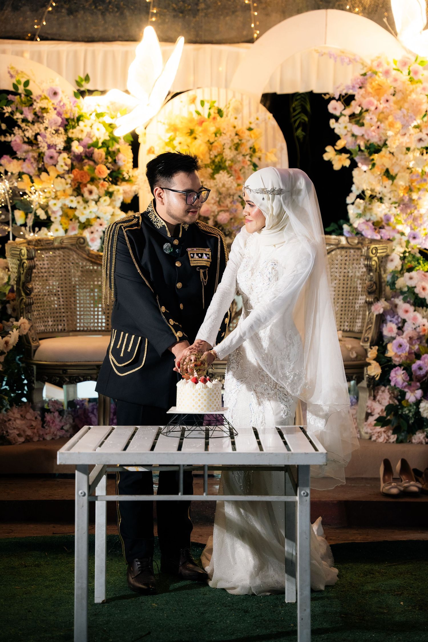 A wedding couple sits on a piano bench surrounded by floral decor, sharing romantic moments in a beautifully lit venue.