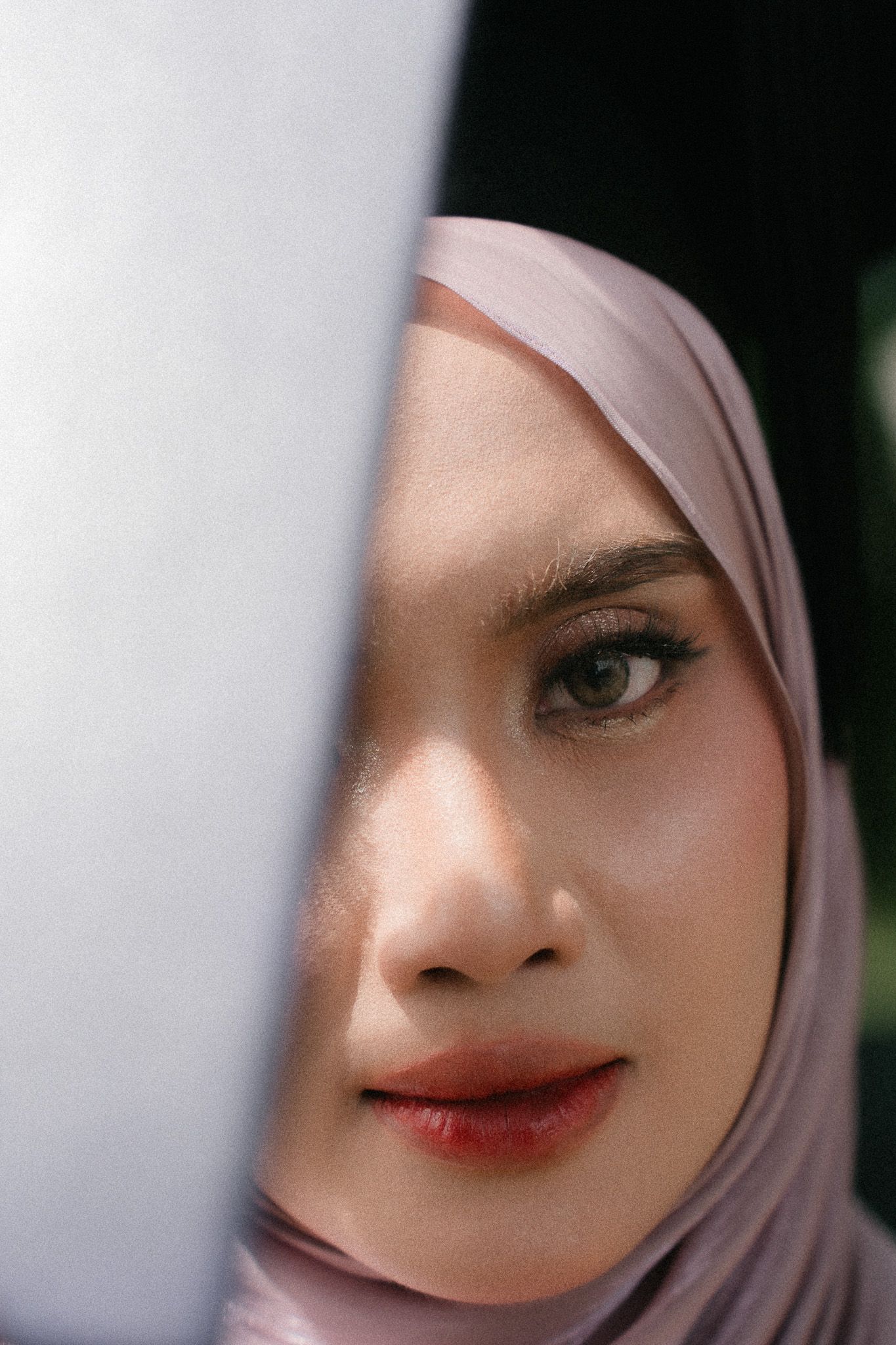 Close-up portrait of a young woman wearing a light pink hijab with subtle makeup and green eyes.