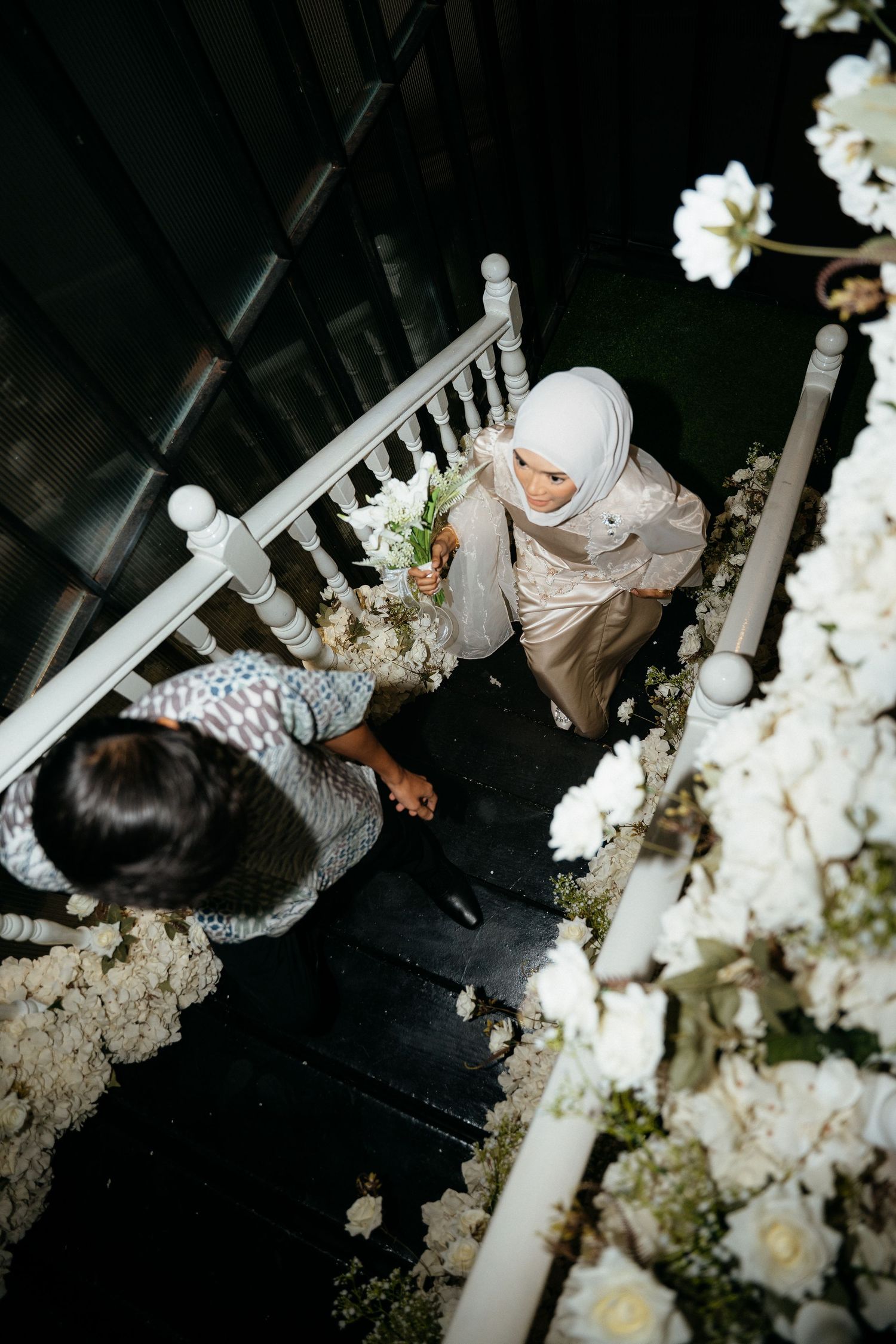 Two people stand on white stairs decorated with elegant white floral arrangements at a formal event.