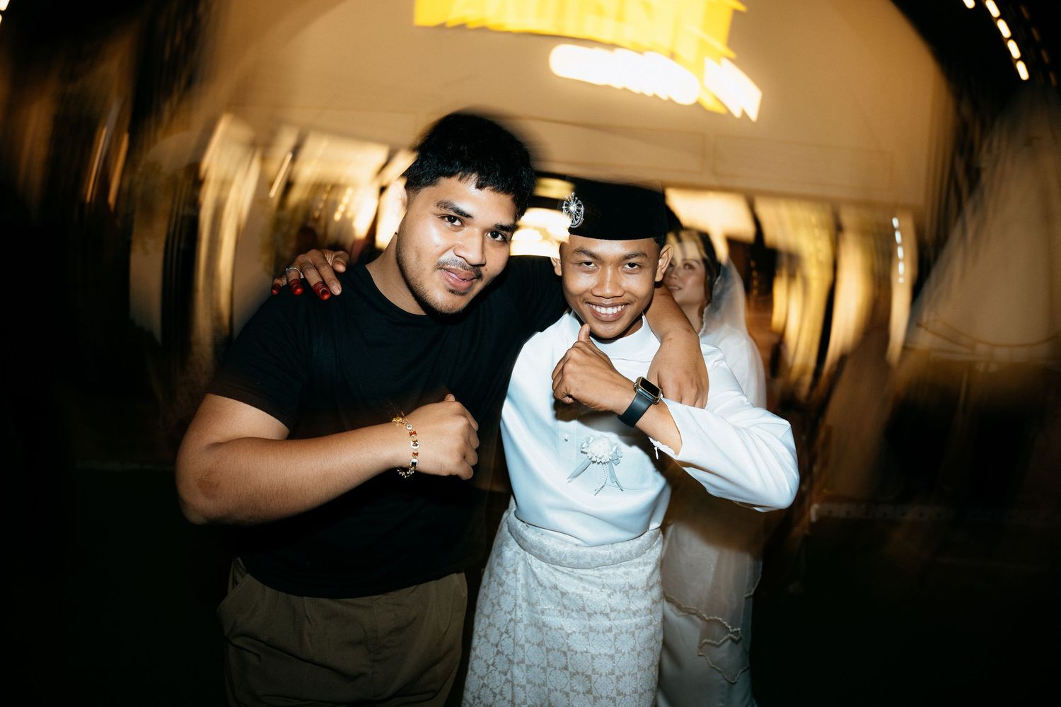 Two people posing together at a club or party venue with blurred lighting in the background.