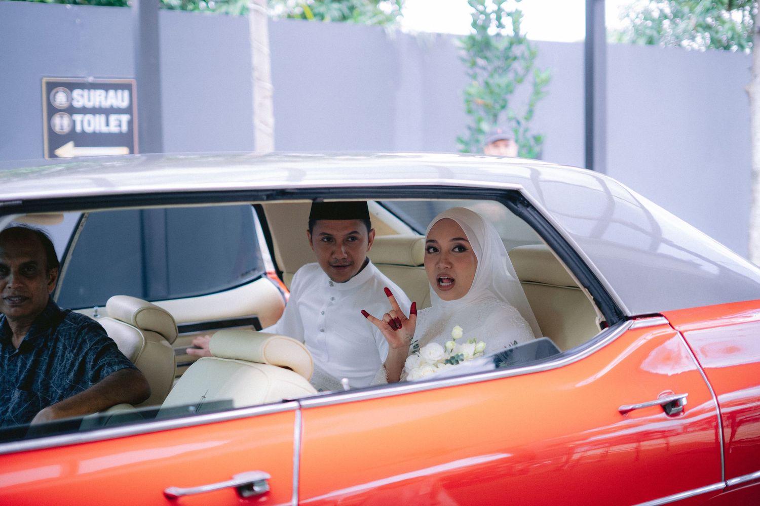 Two passengers sit in a vintage orange car in a color photograph.