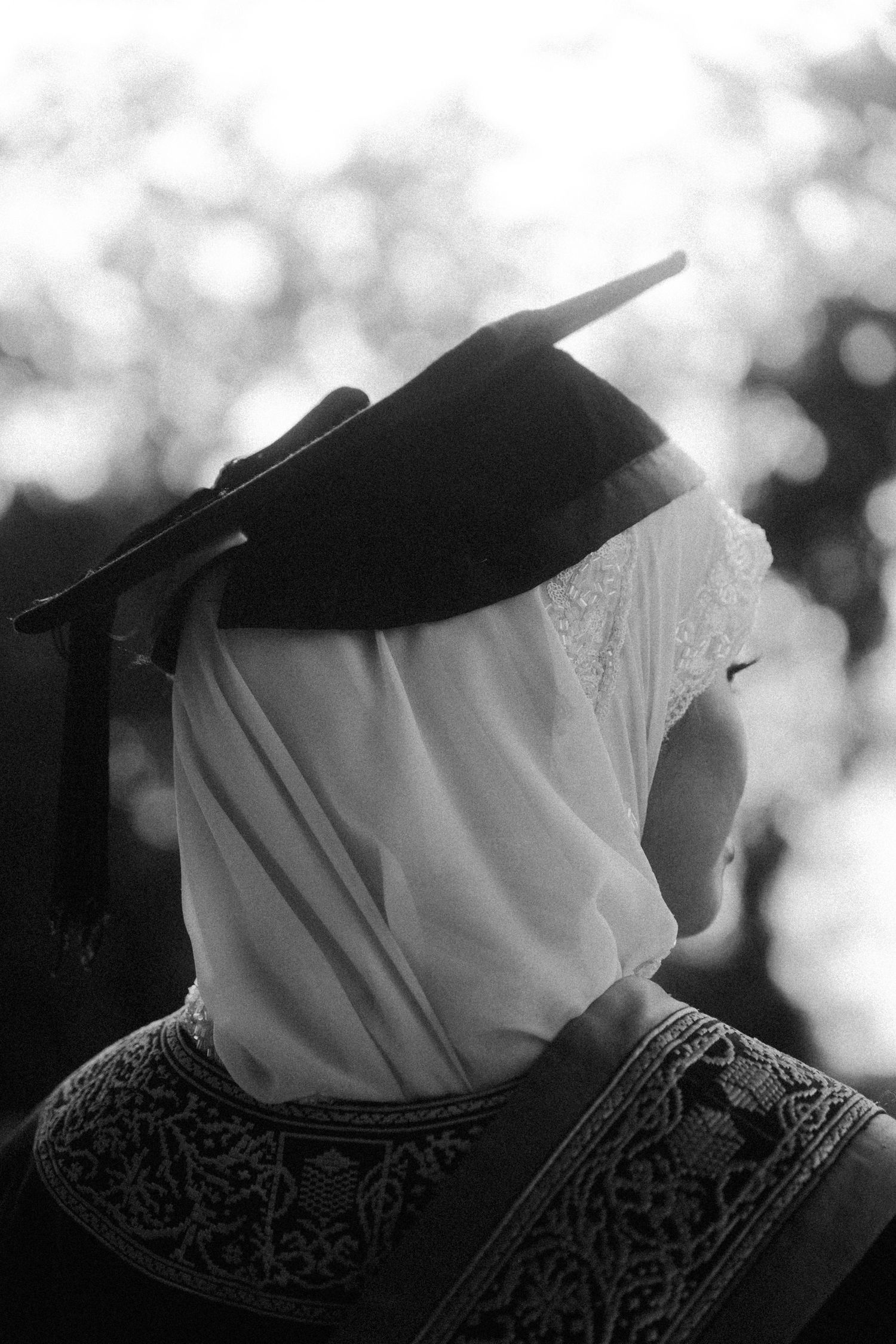 A black and white profile view of a person wearing a graduation cap and ornate patterned clothing.