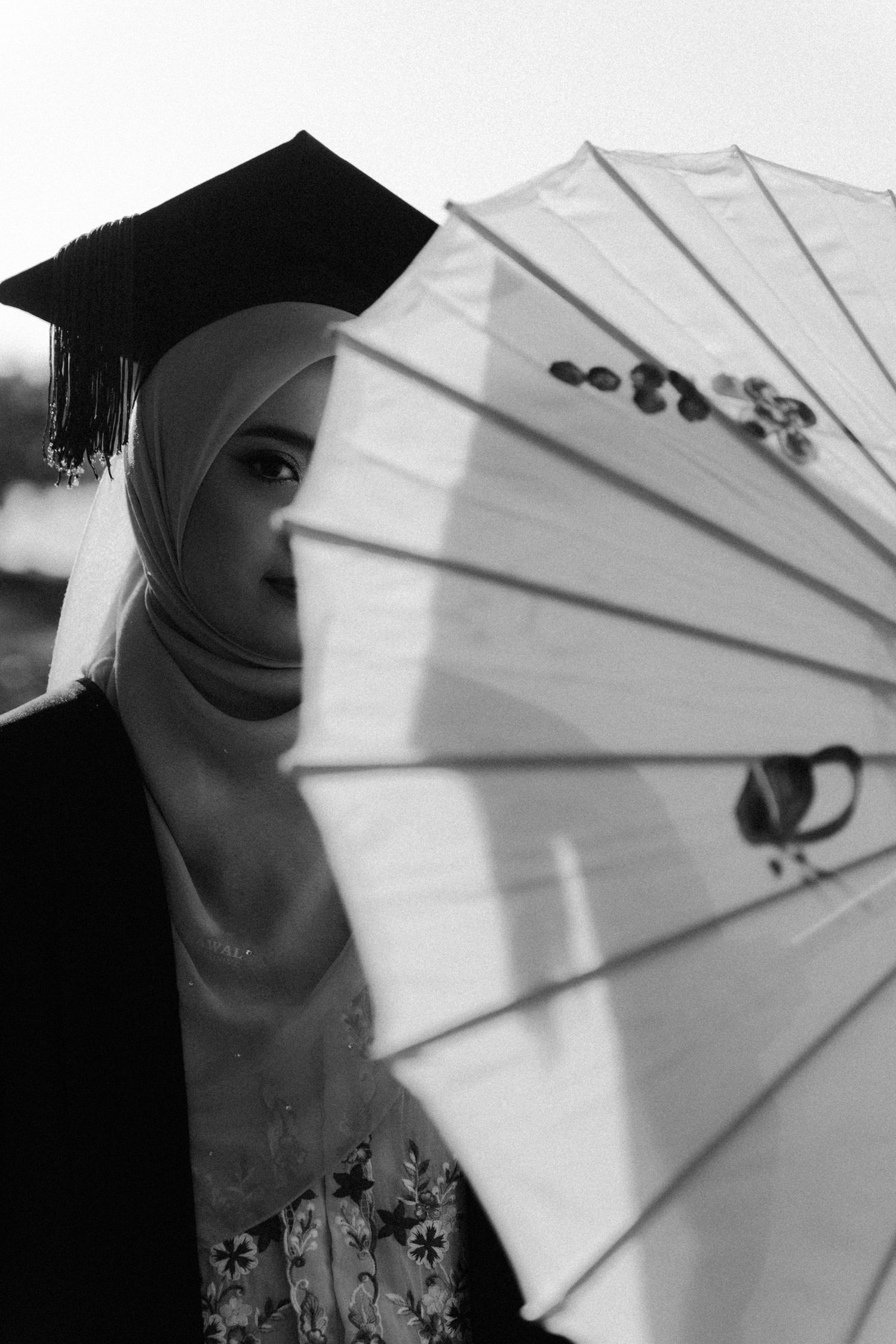 A series of black and white photos showing someone posing with a decorative white paper parasol in different angles.