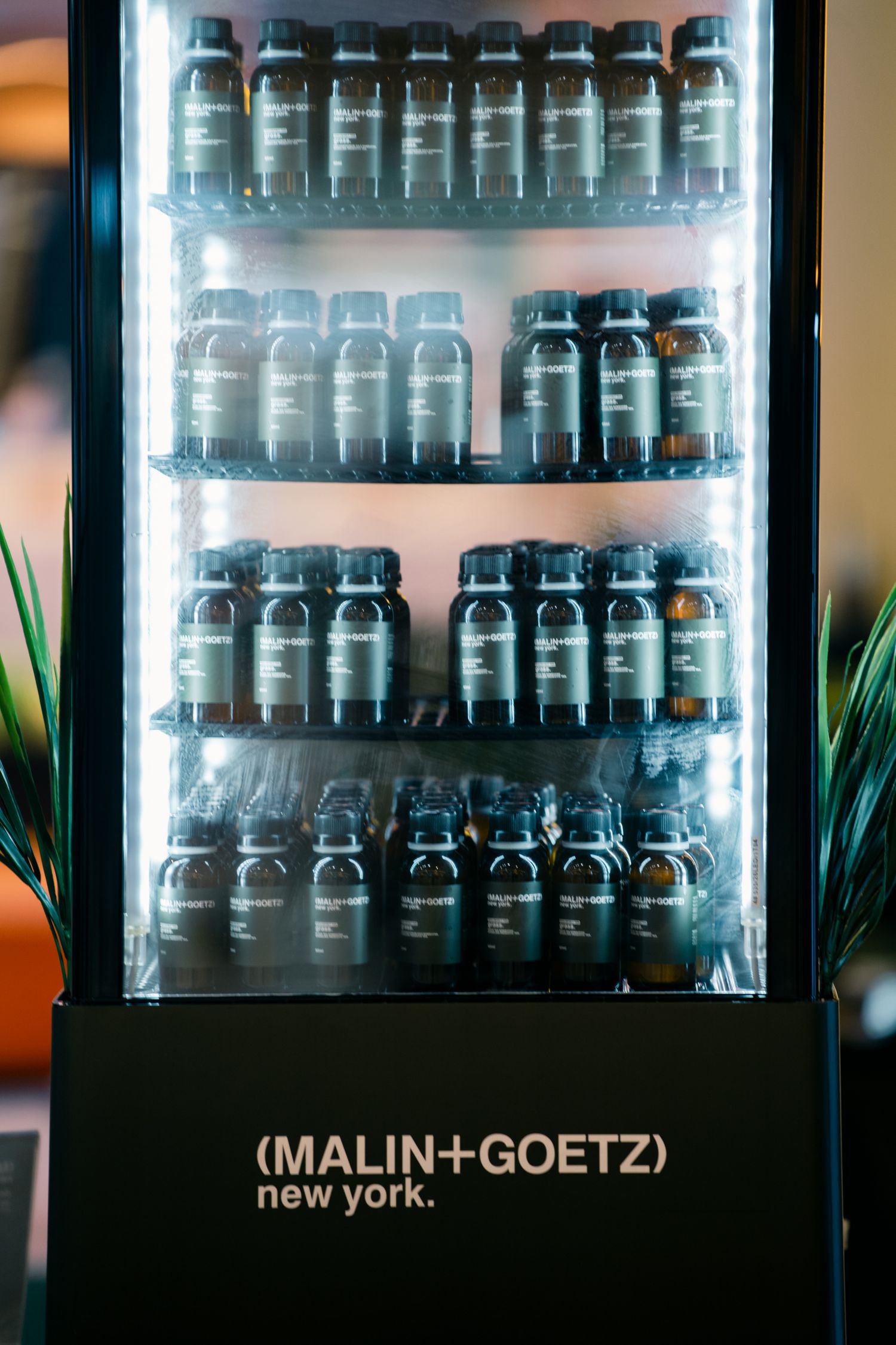 Refrigerated display case filled with Malin+Goetz branded bottles on multiple shelves.