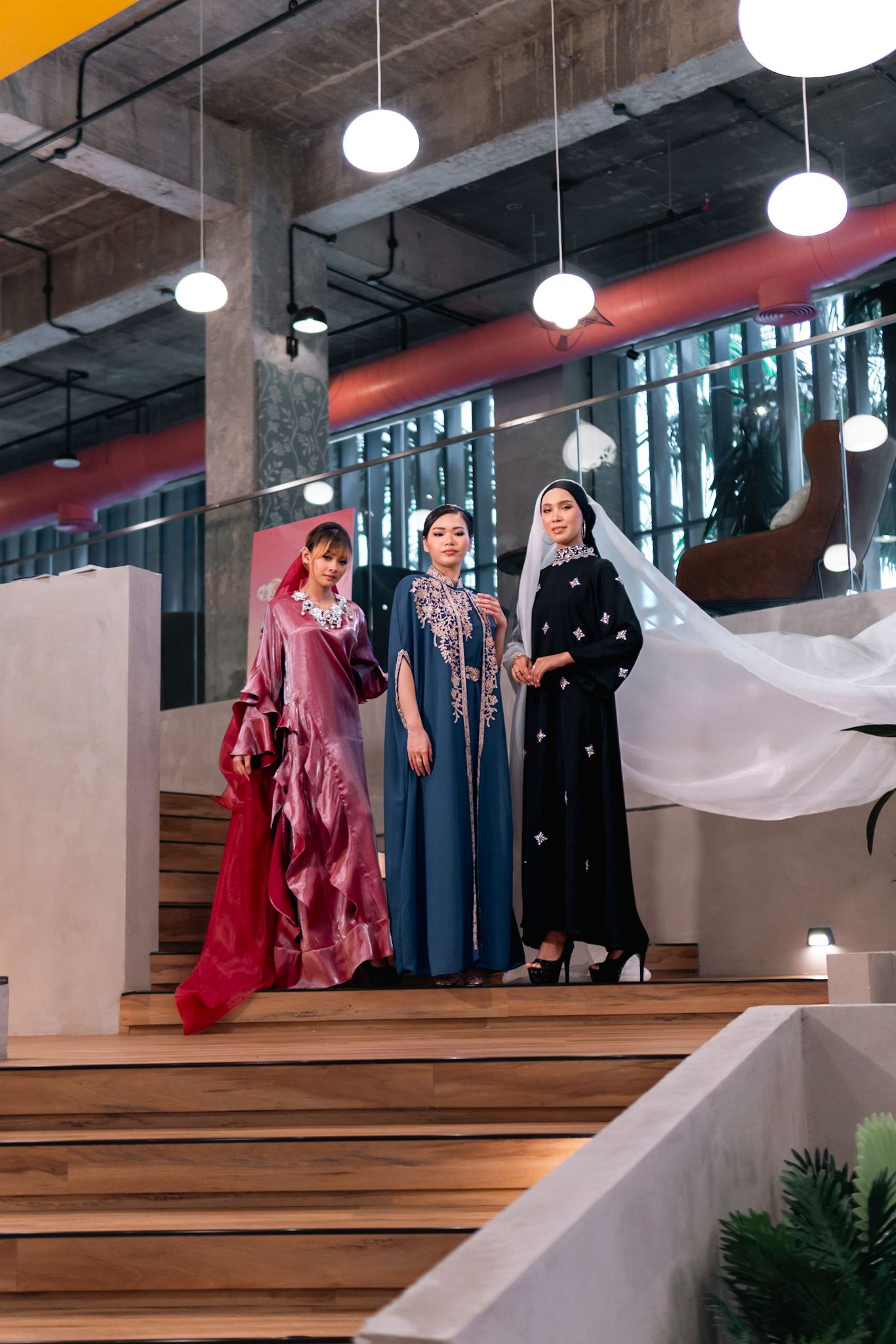 Three elegant dresses in red, blue, and black with flowing fabric on modern wooden staircase.