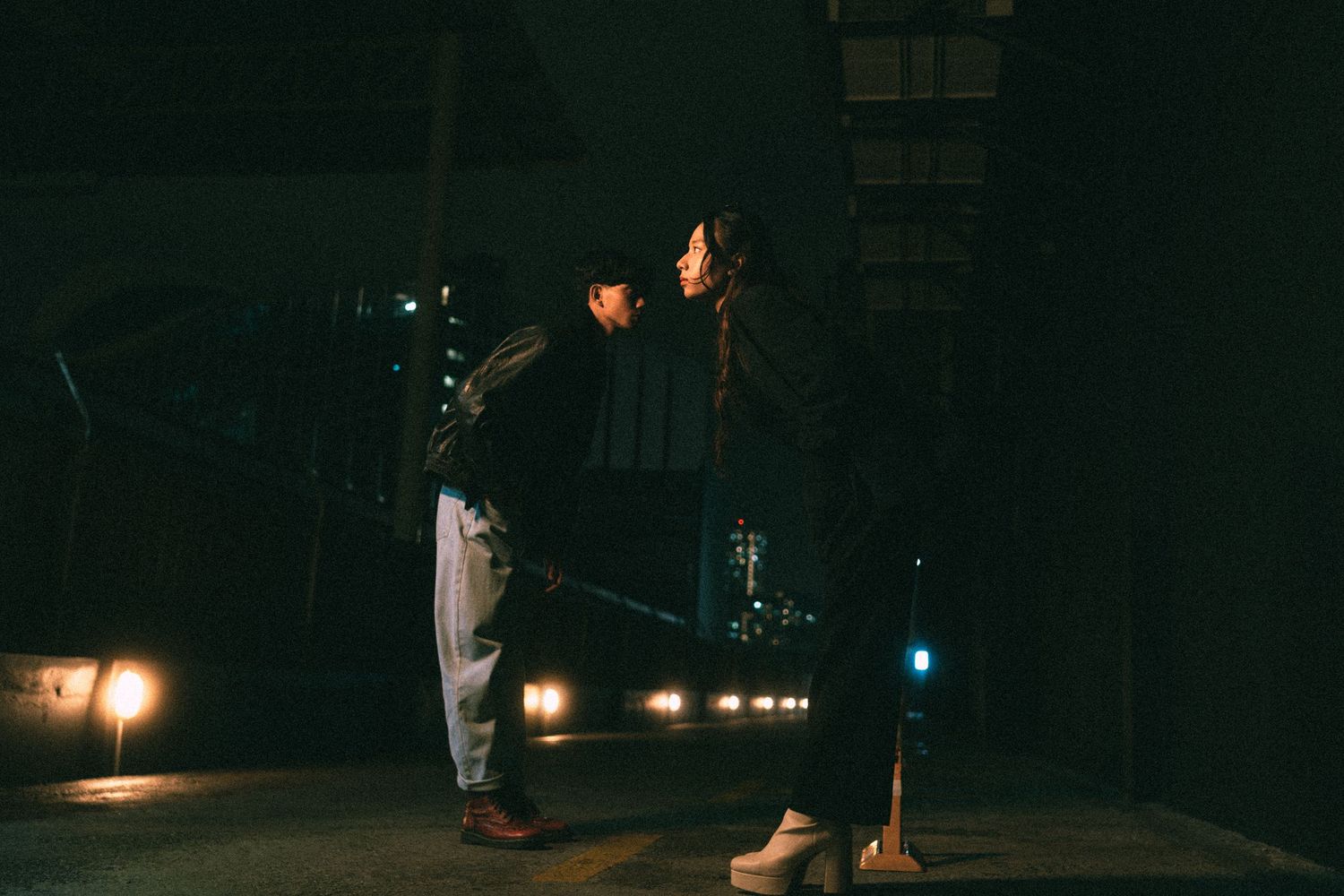 Two people standing in dramatic poses against a dark urban nighttime setting.