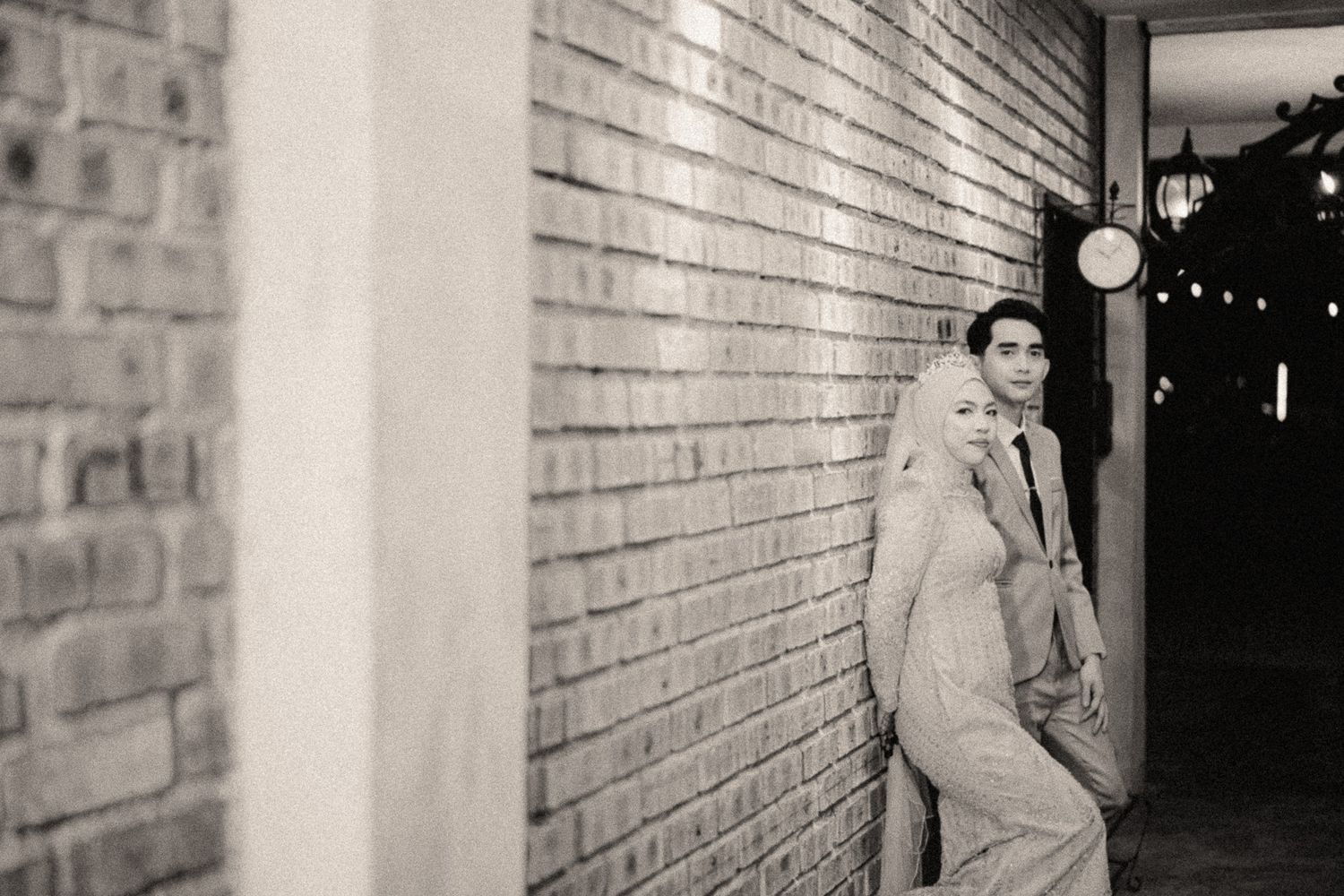 A couple poses romantically against a brick wall in a black and white engagement photo at night.
