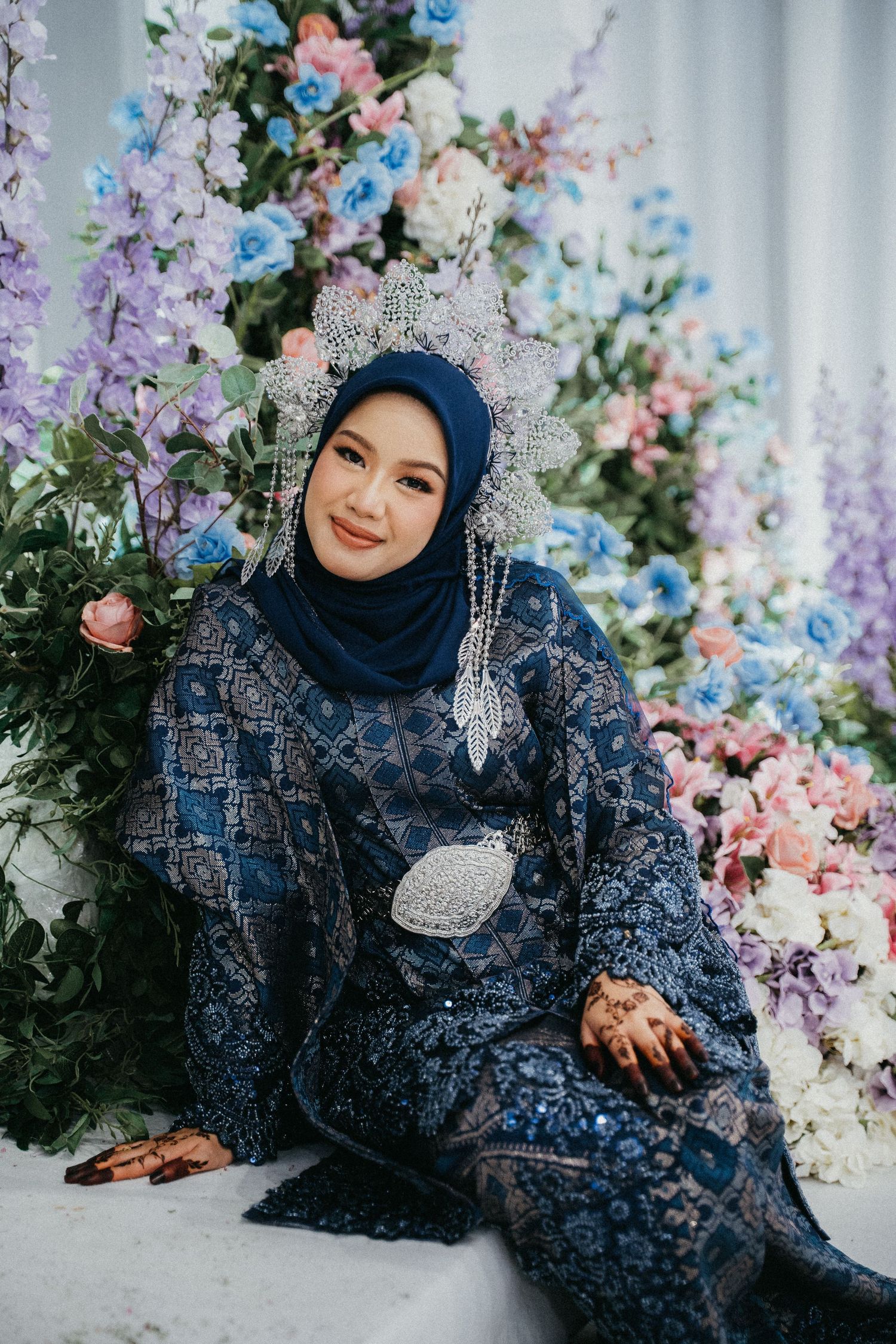 Person in a navy blue lace dress poses gracefully against a backdrop of colorful pastel flowers.