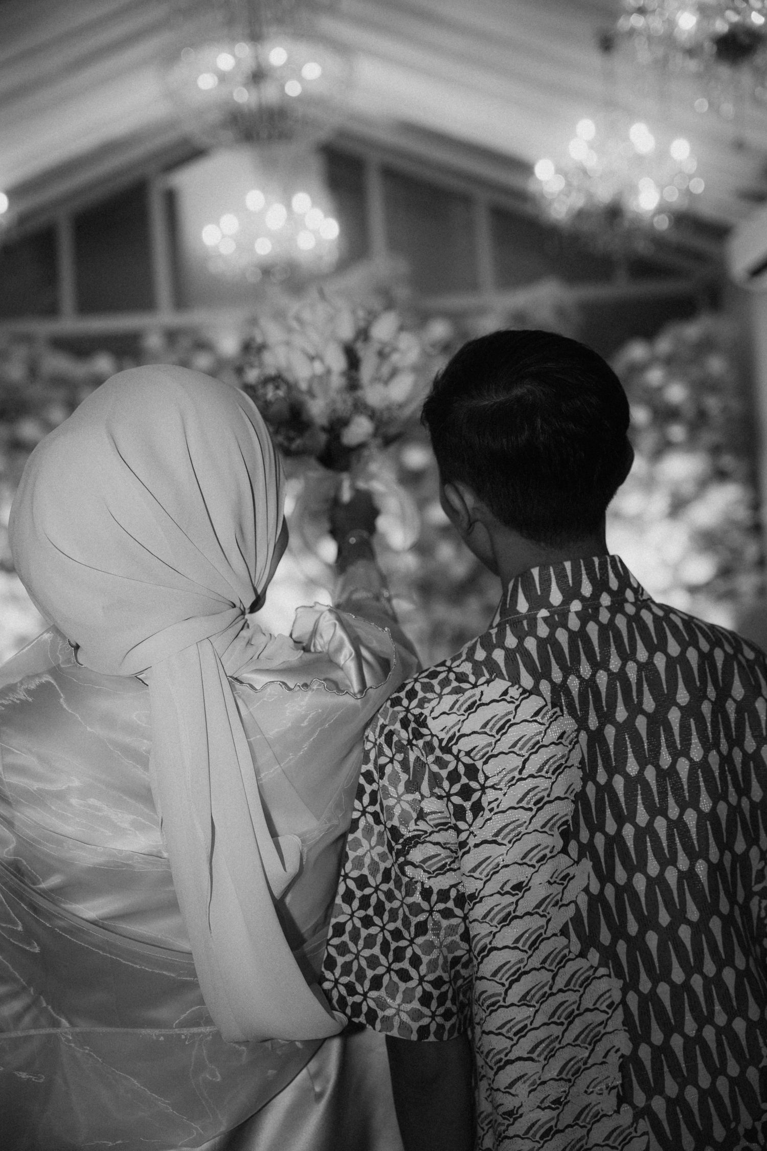 A black and white photo series shows a couple in formal attire having a dance moment under chandeliers.