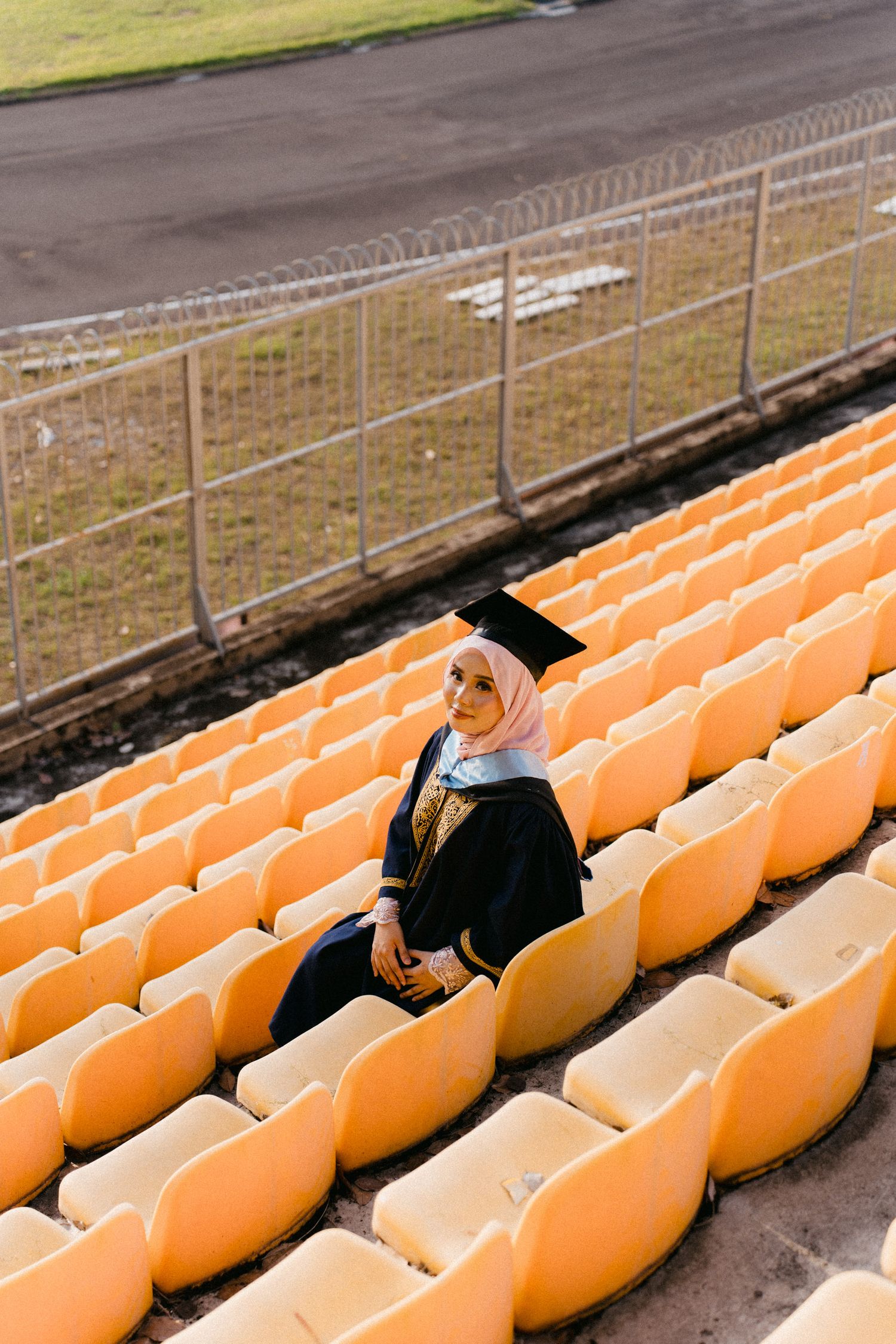 Orange stadium seats arranged in rows on concrete bleachers with a dirt field visible below.