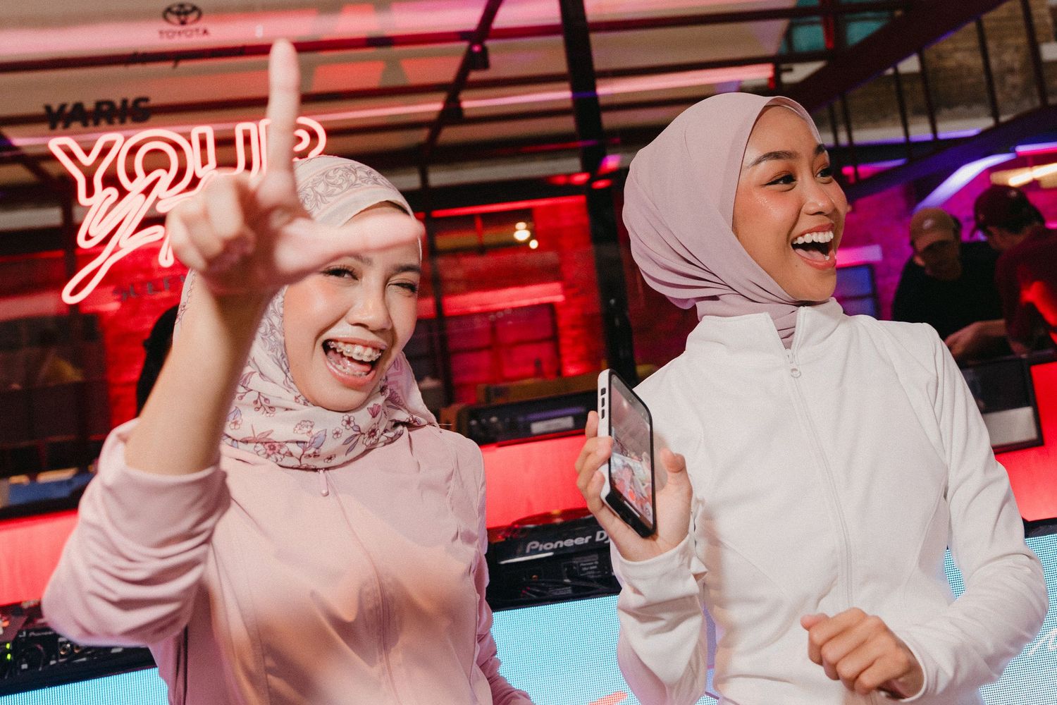 A person in a white hijab laughs joyfully in a room with red ambient lighting.