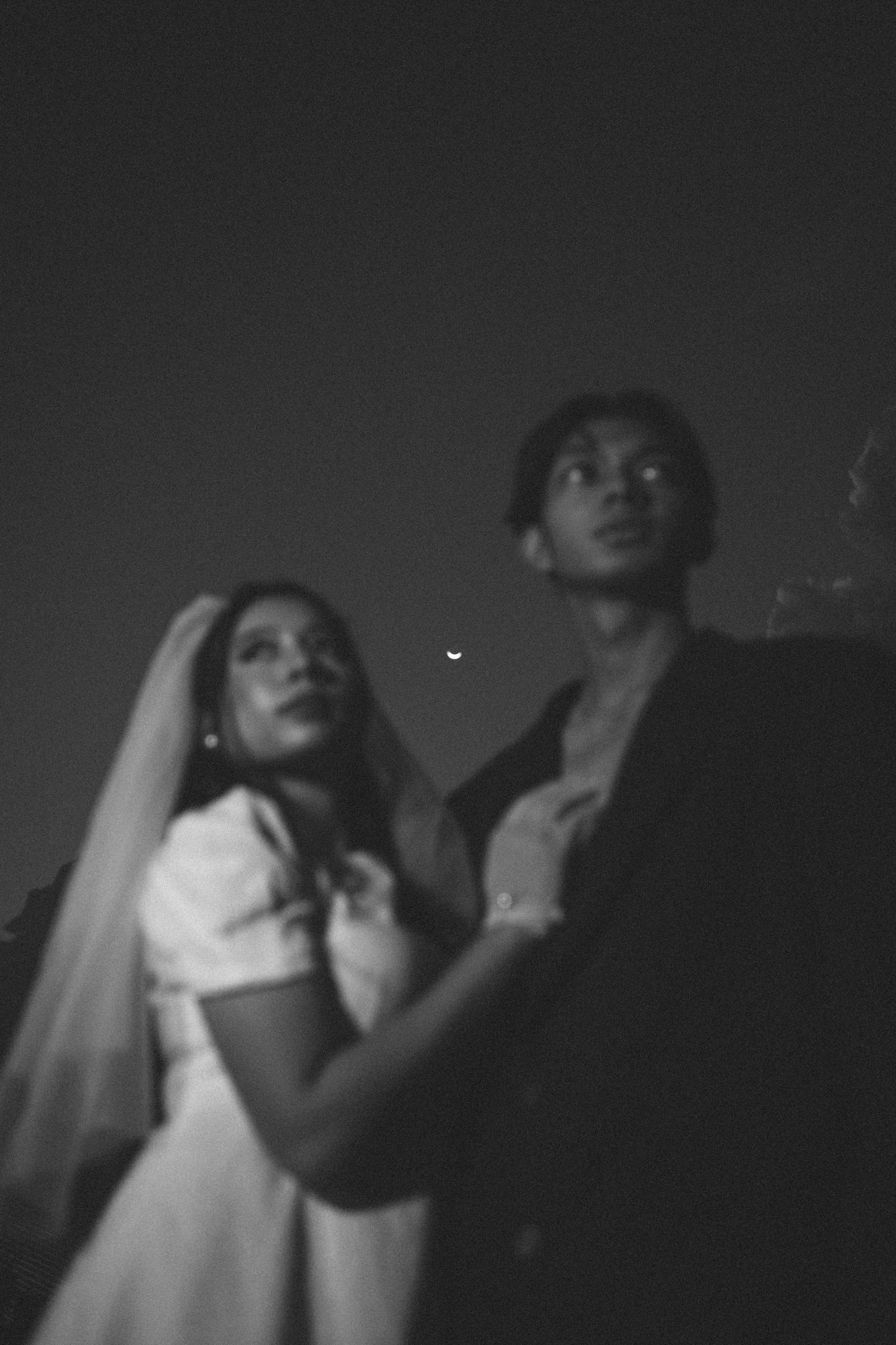 Black and white photo of couple in wedding attire against night sky.
