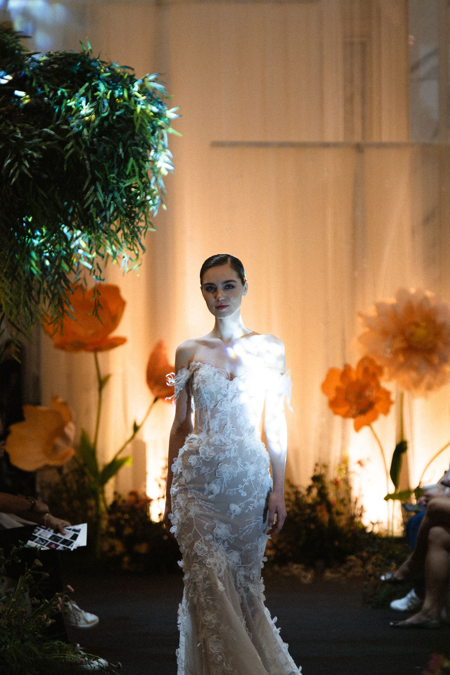 Wedding dress fashion show with dramatic lighting and orange floral decorations.