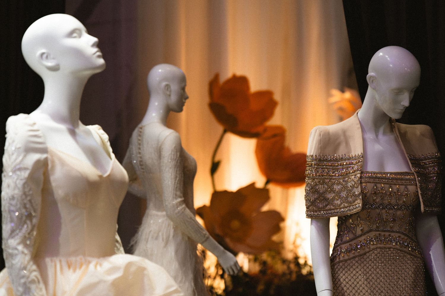 White mannequins displaying elegant wedding dresses with orange floral backdrop.