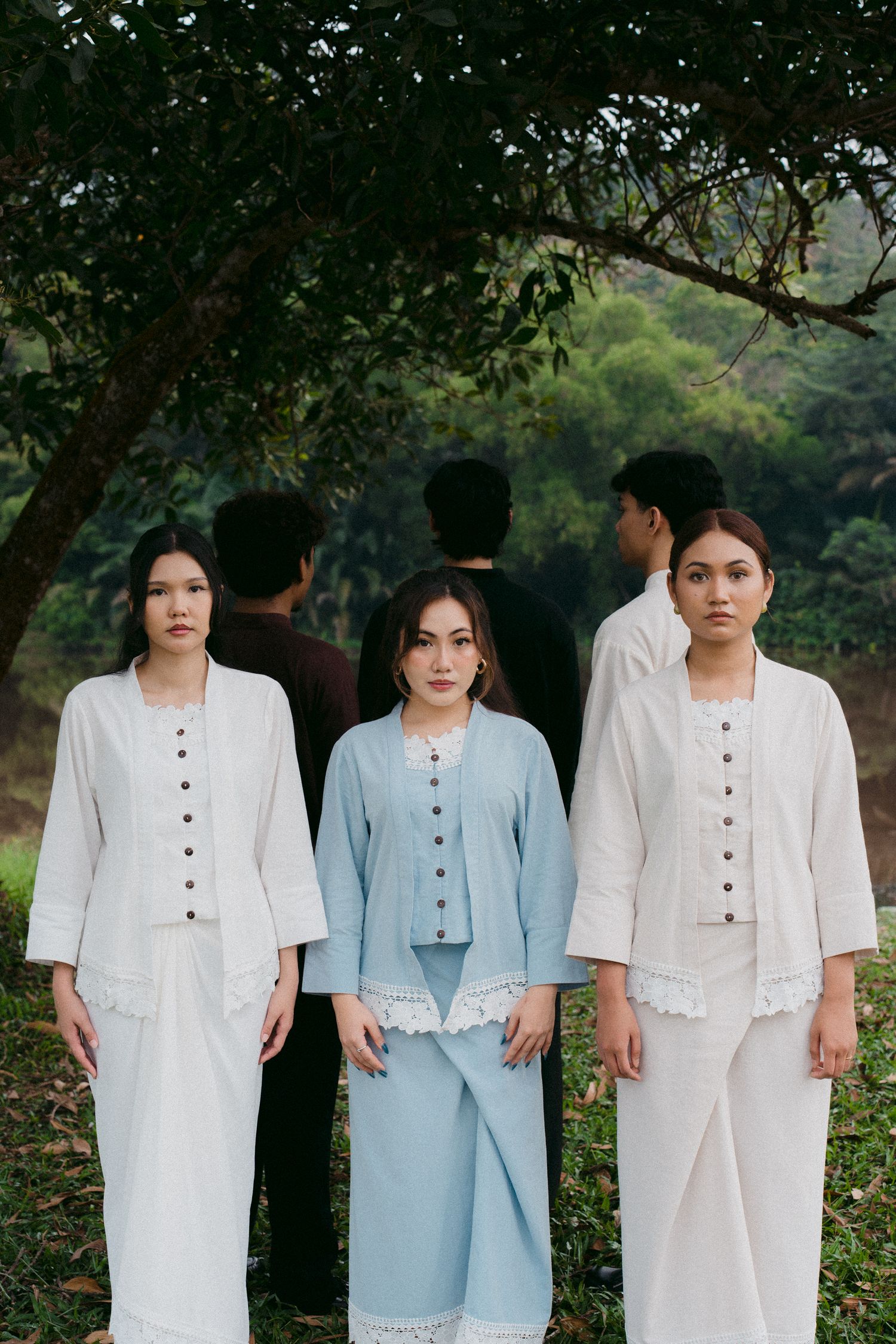 Three models in coordinated white and blue button-front outfits posed outdoors.