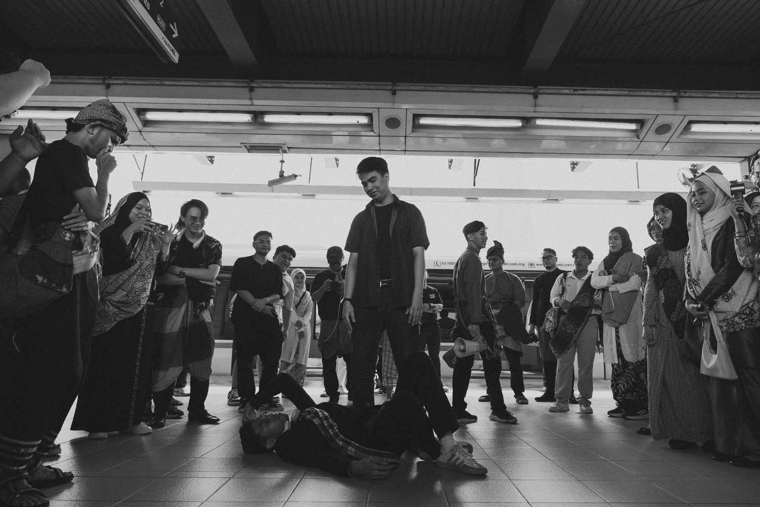 Black and white photo of crowd gathered around performers in indoor space.