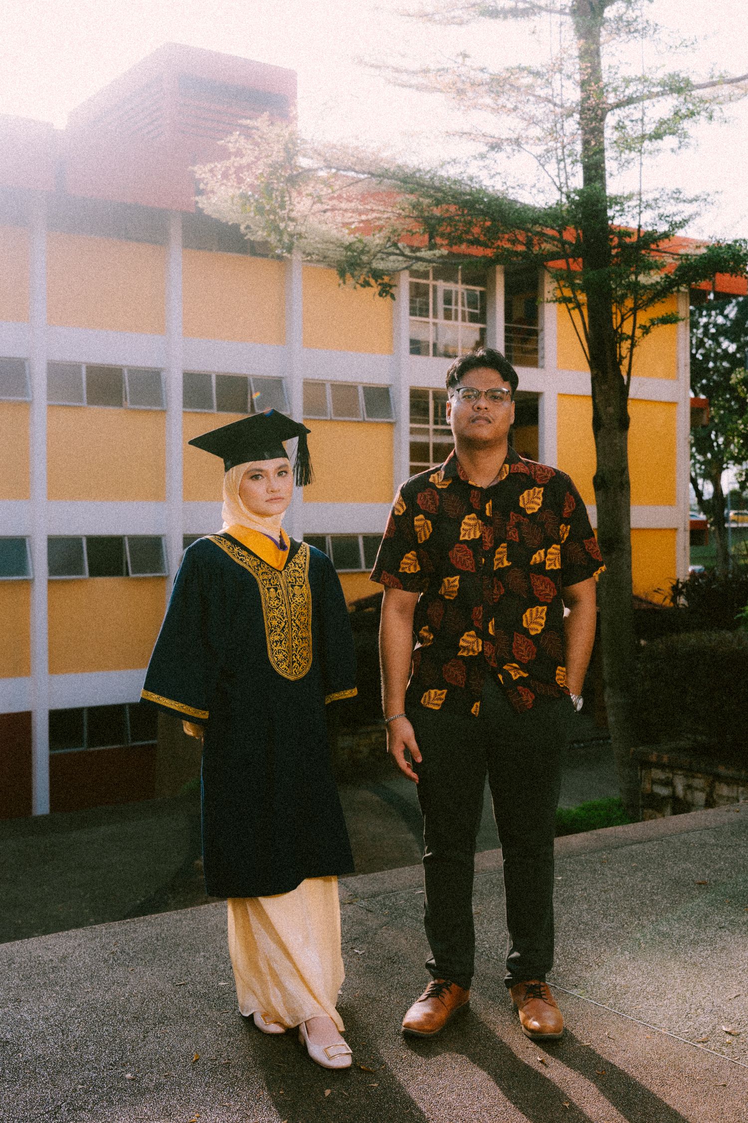 People pose together outside a yellow school building during a graduation ceremony.