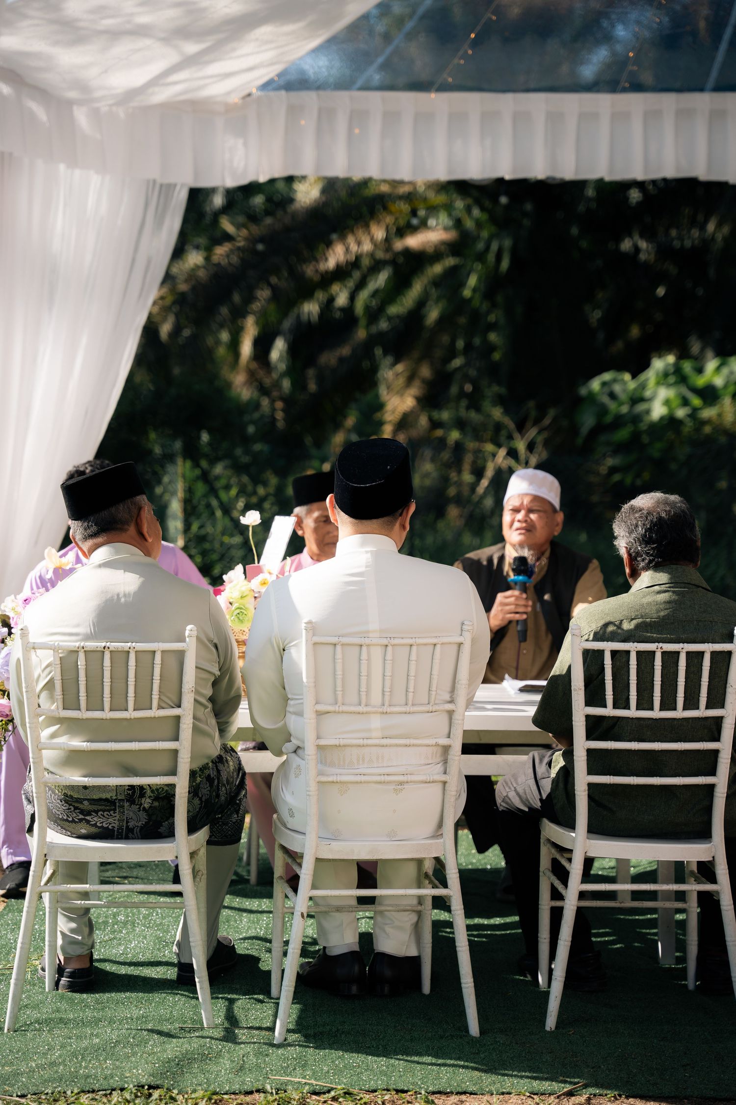 A group sits at a white-clothed table under an outdoor wedding tent, gathered together during an intimate ceremony.