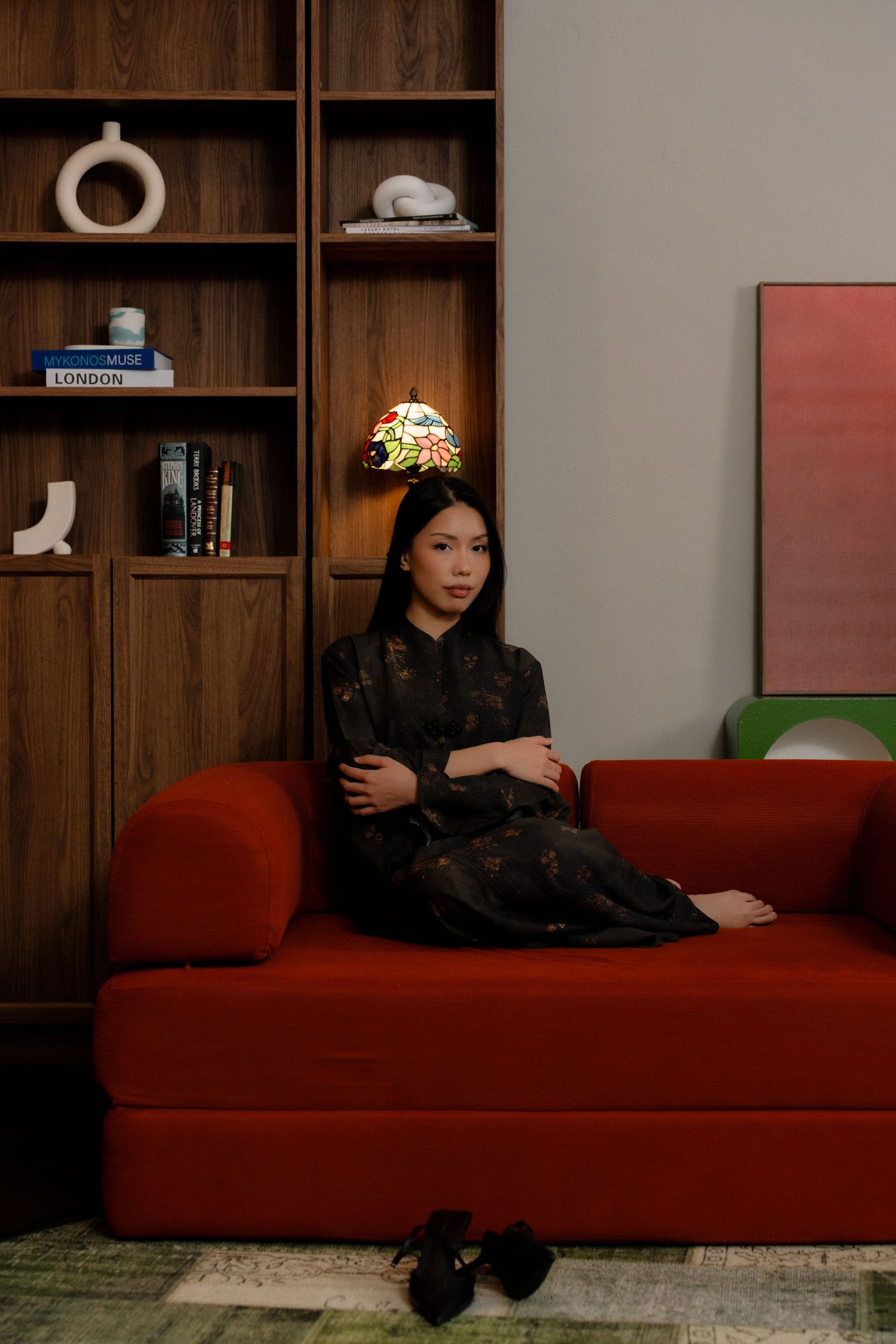A black cat lounges on a red couch in a modern living room with wooden shelving and decor.