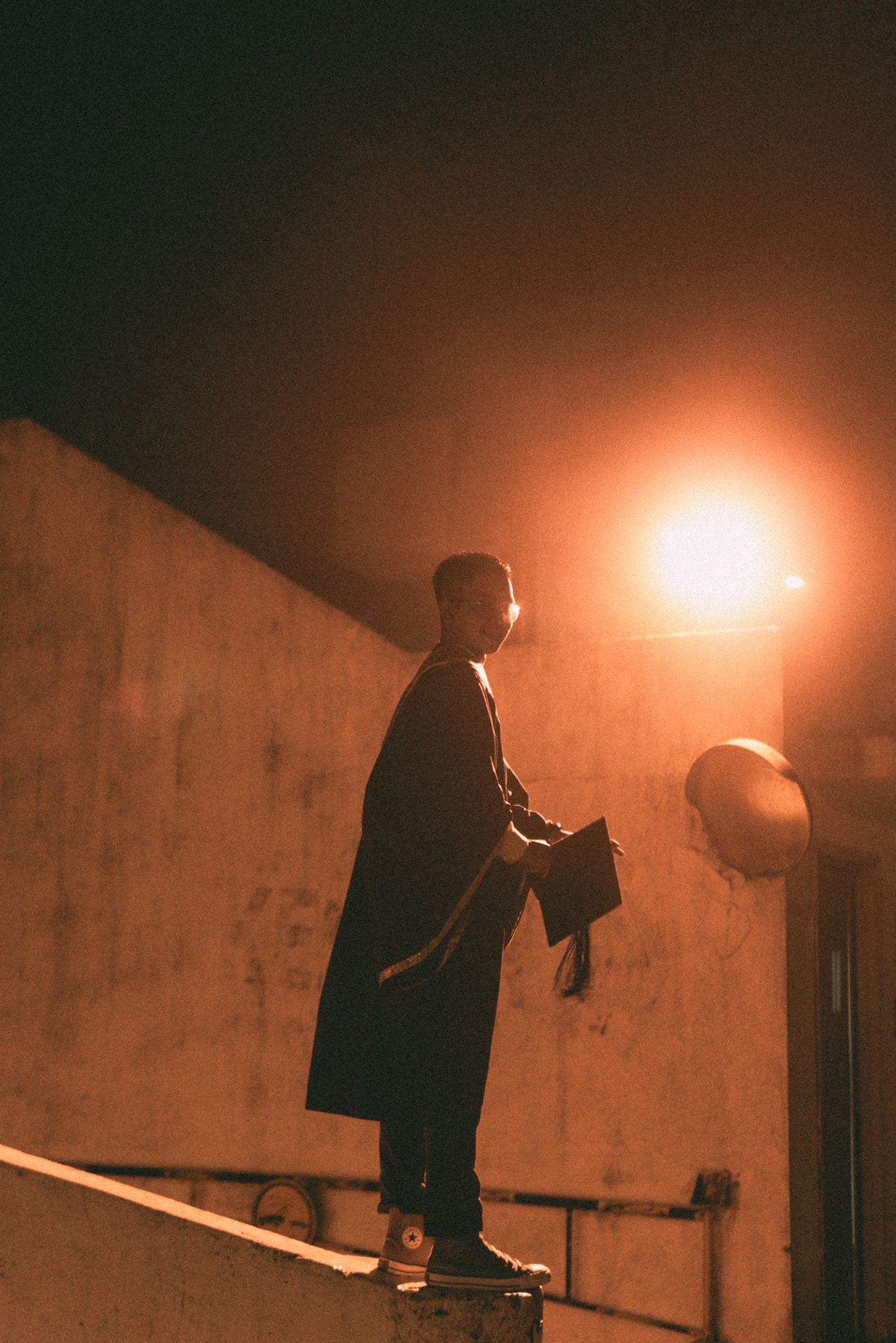Silhouette of person standing against wall with dramatic orange lighting at night.
