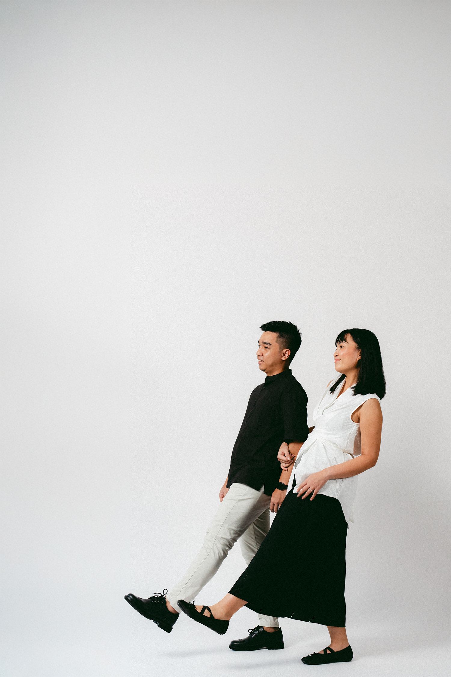 A minimalist fashion portrait of two people in contrasting black and white outfits walking in profile.