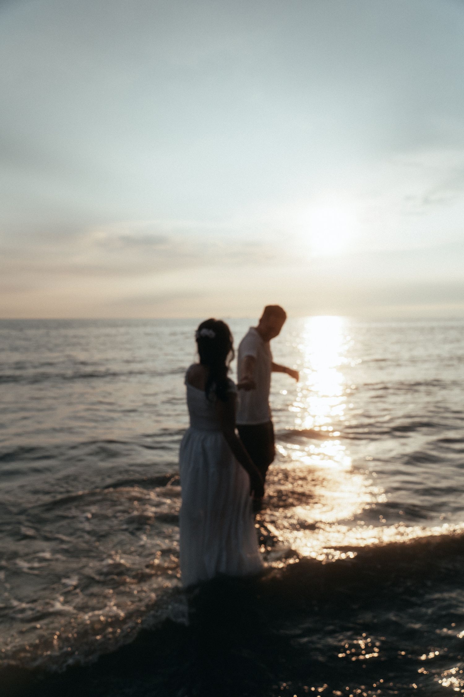 A couple standing in ocean water silhouetted against a setting sun.