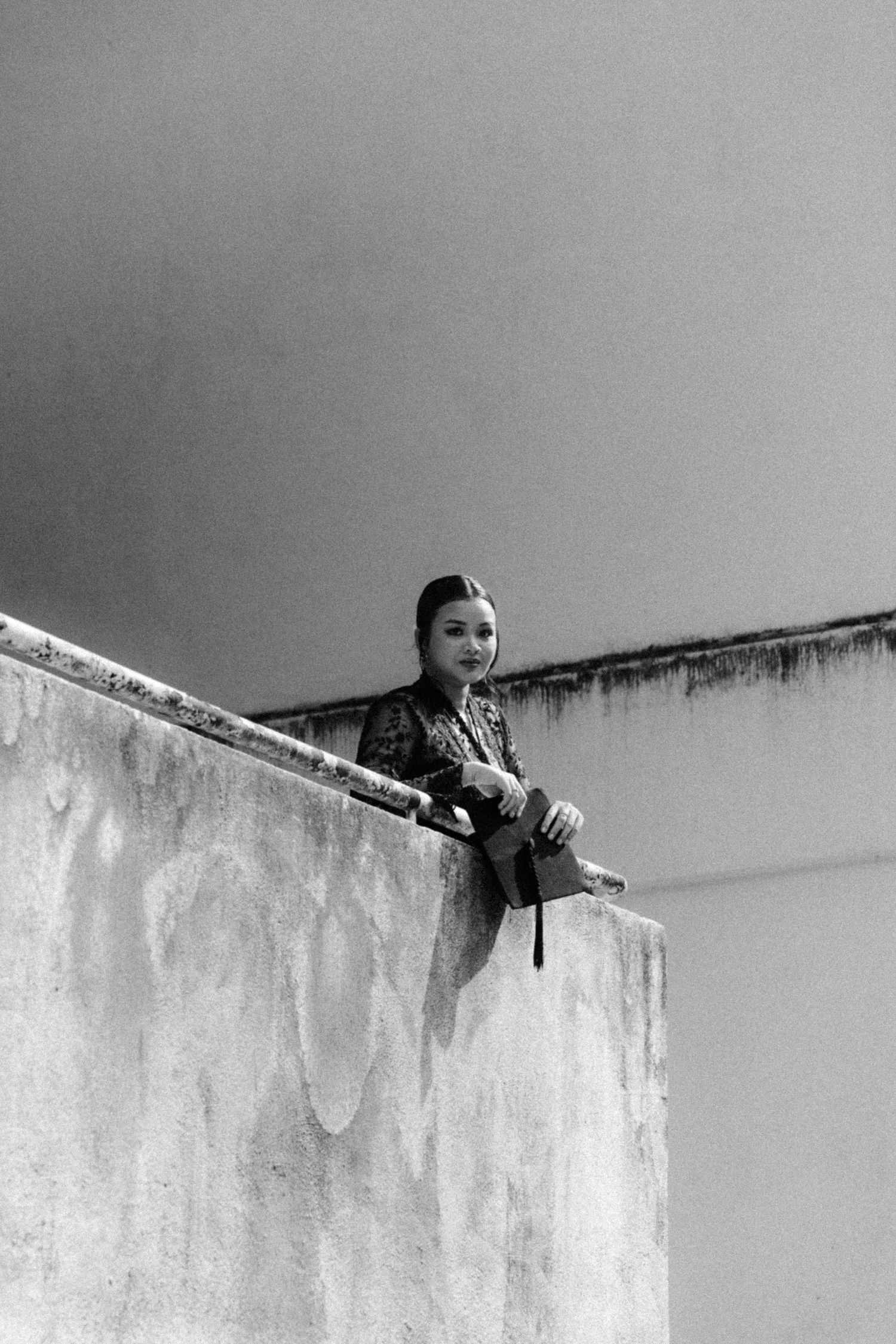 A figure in black looks down from atop a white concrete wall in an artistic black and white photograph.