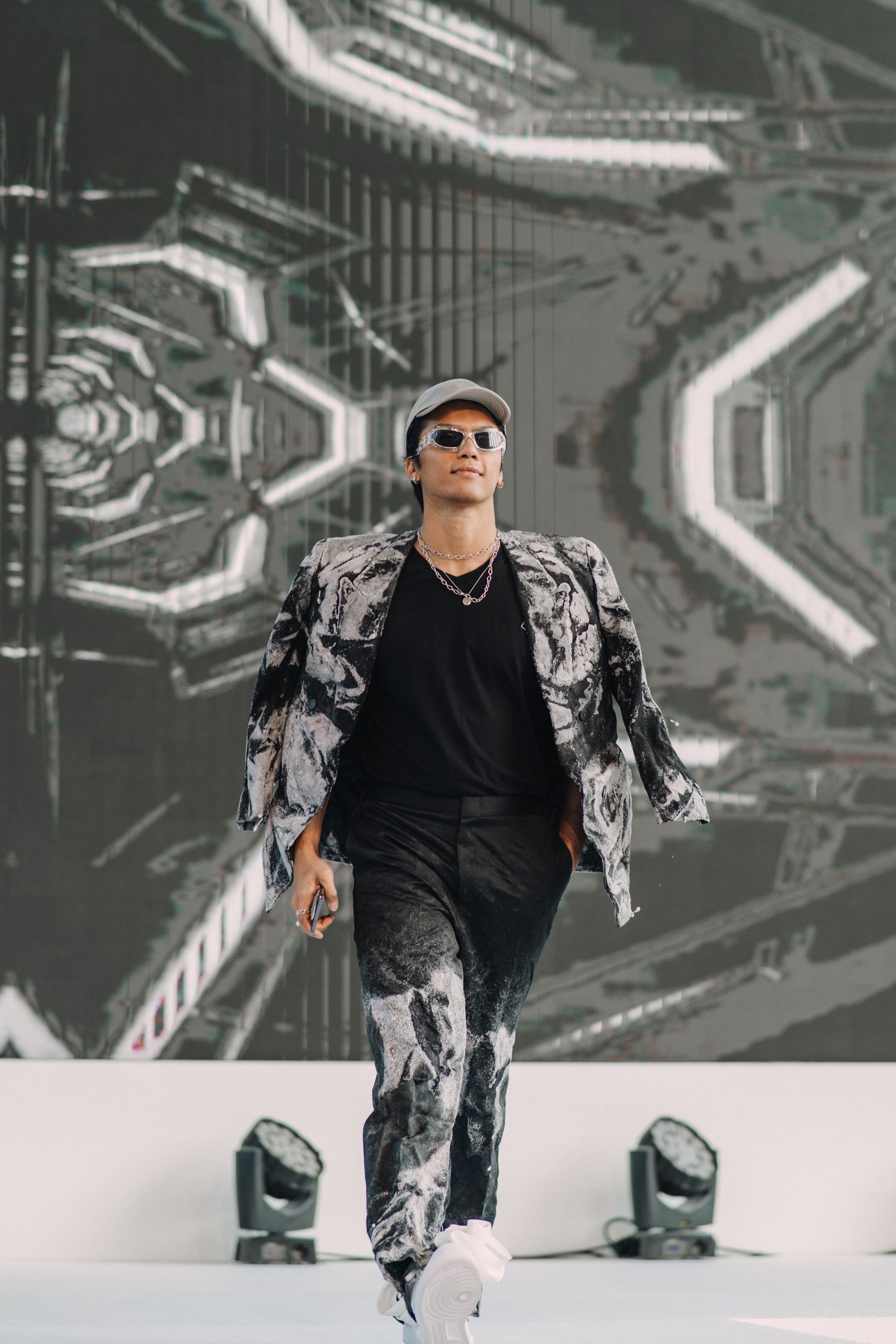 Model walks runway in black and white patterned outfit on futuristic stage with geometric backdrop.