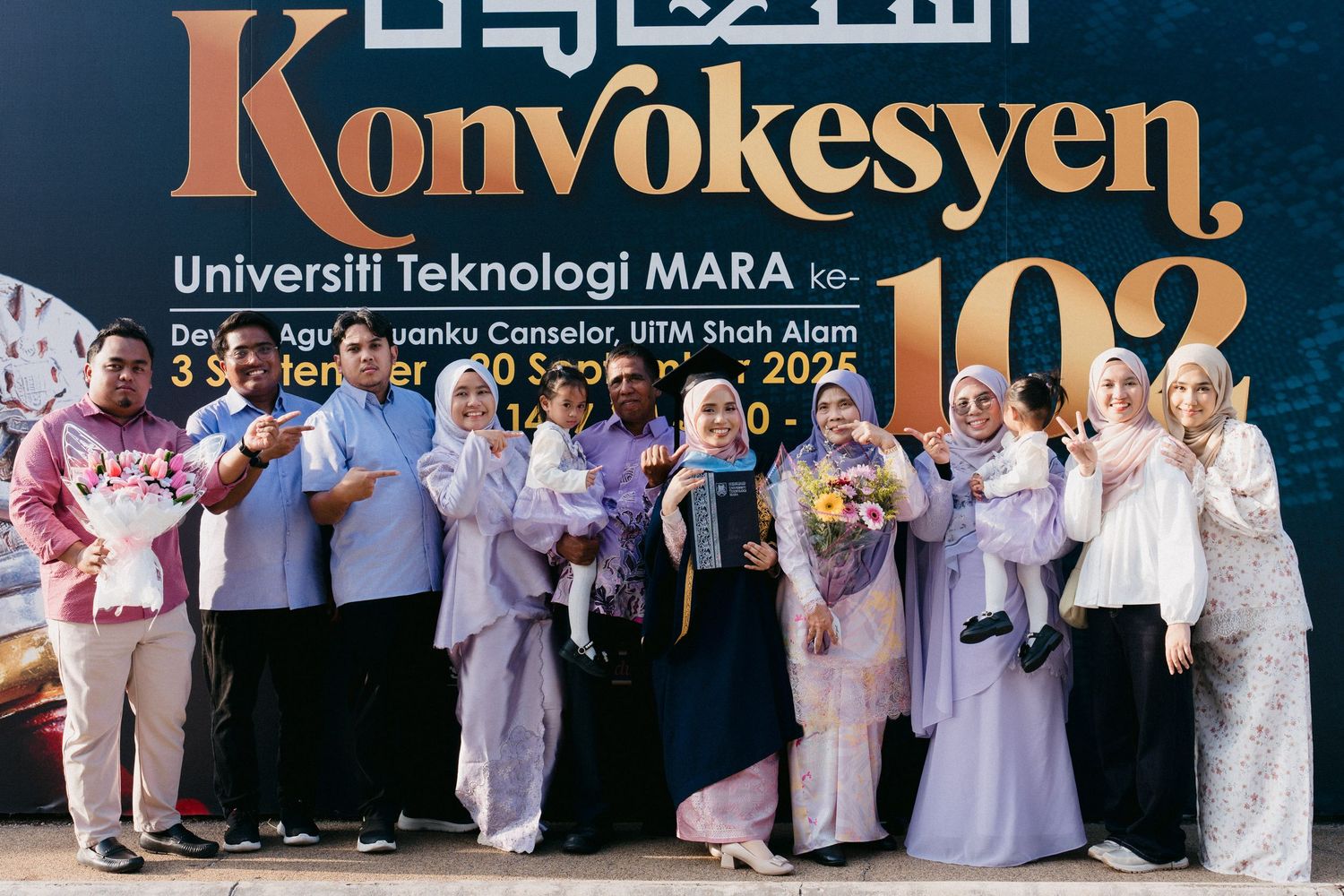 A group of graduates in formal attire pose together holding bouquets at a university convocation ceremony.