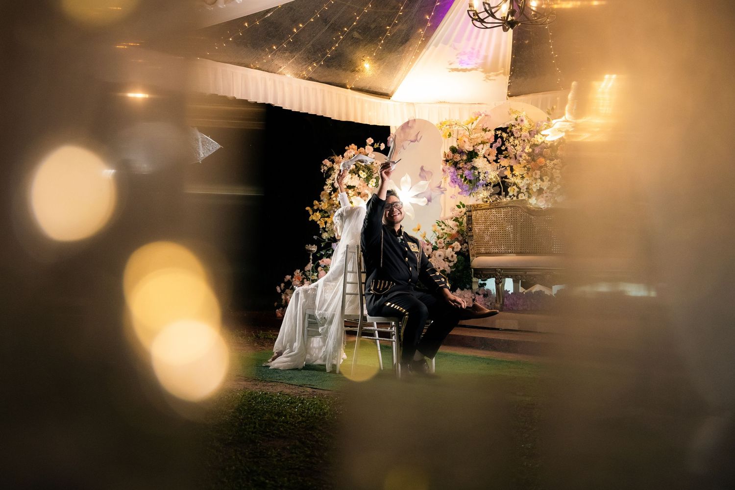 Creative wedding photograph captured through glass with blurred bokeh lights and dancing couple in the distance at night.