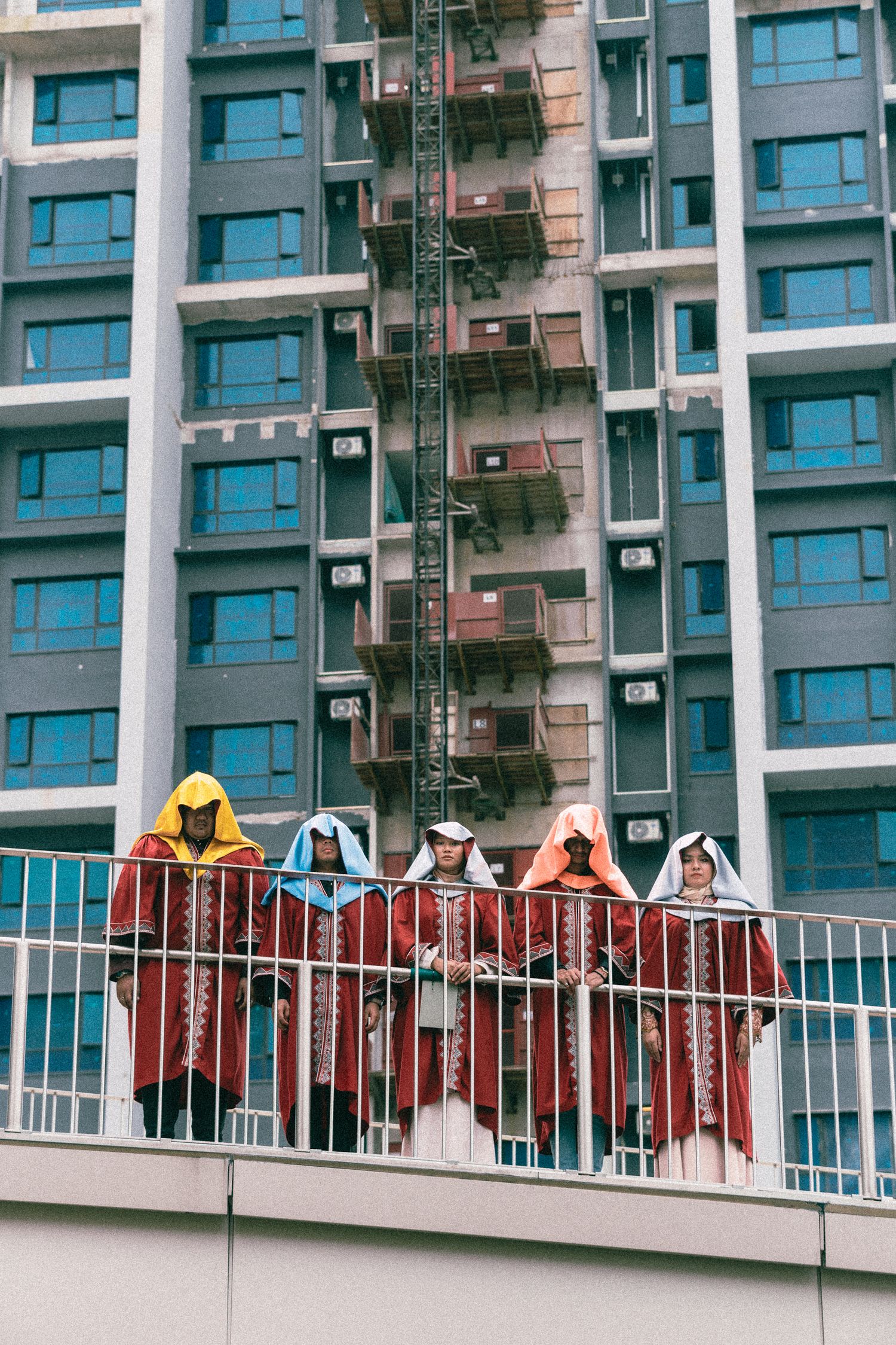 Graduates in colorful regalia pose on a balcony against modern apartment building.